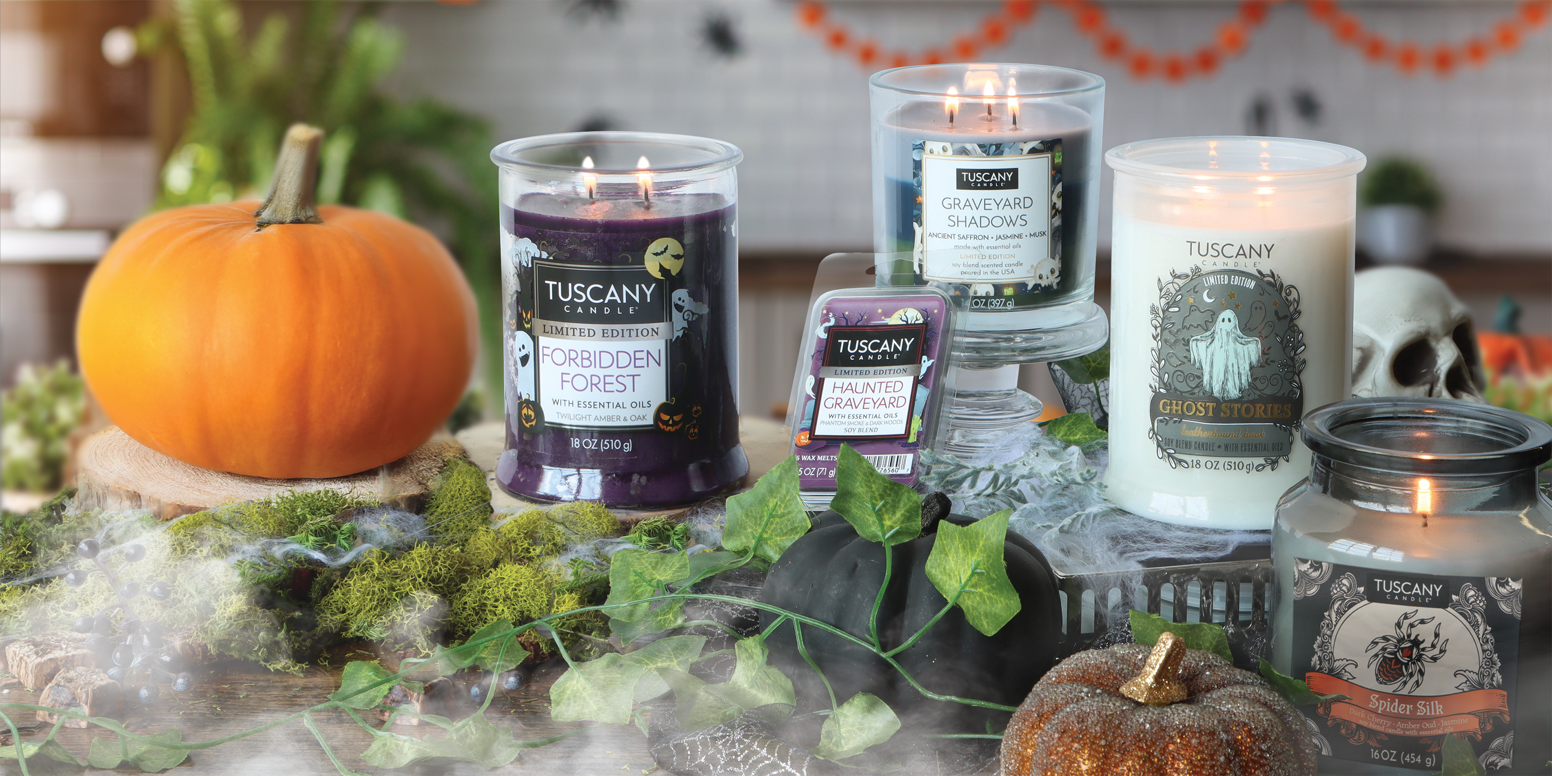 A Halloween-themed display with Tuscany Candle products, a pumpkin, artificial moss, a black ceramic pumpkin, a glitter pumpkin, and festive decorations in the background.
