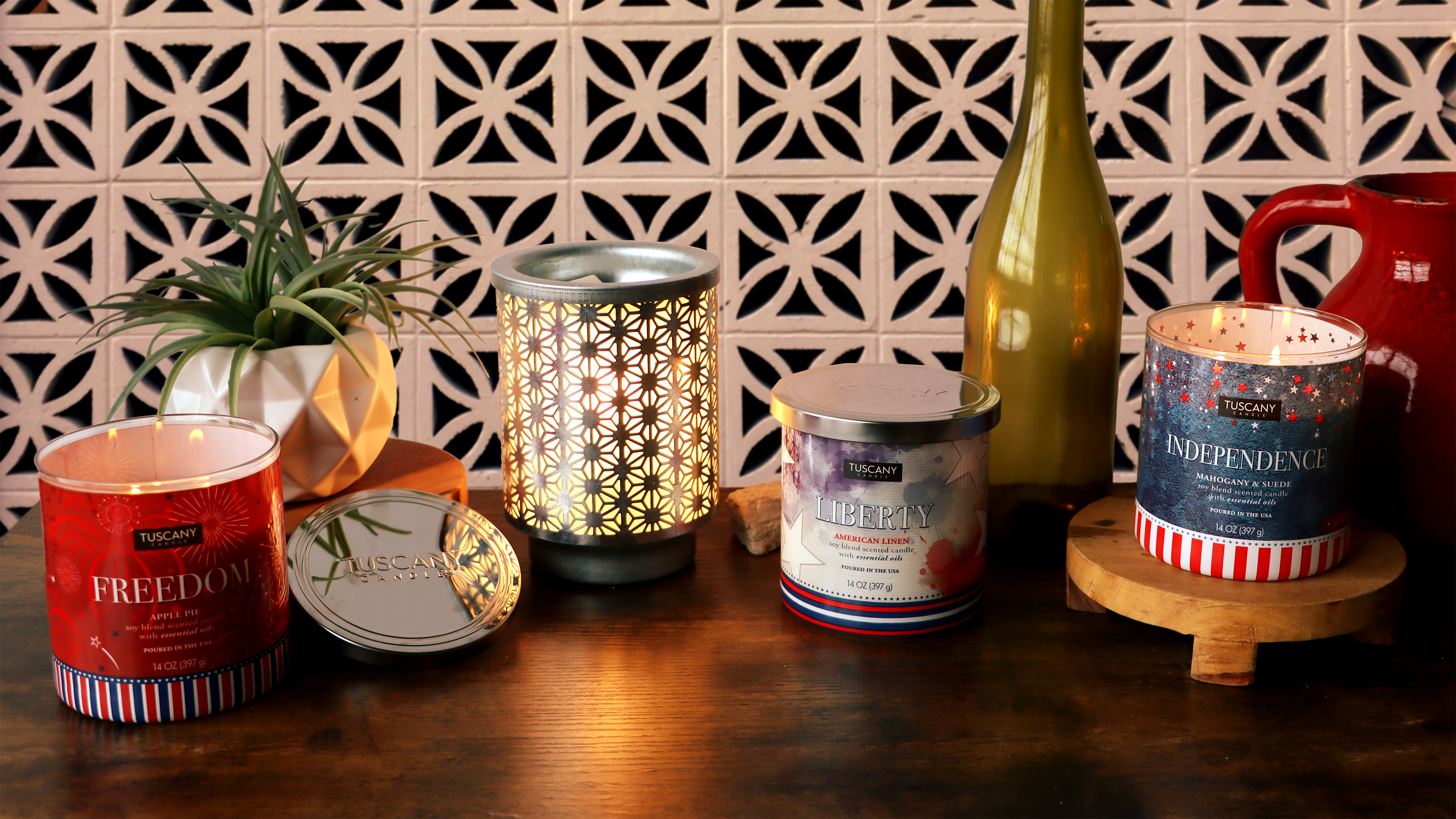 Four Tuscany Candle jars with citrus and mango scents are displayed on a wooden surface with oranges, a mango, and green leaves in the background.