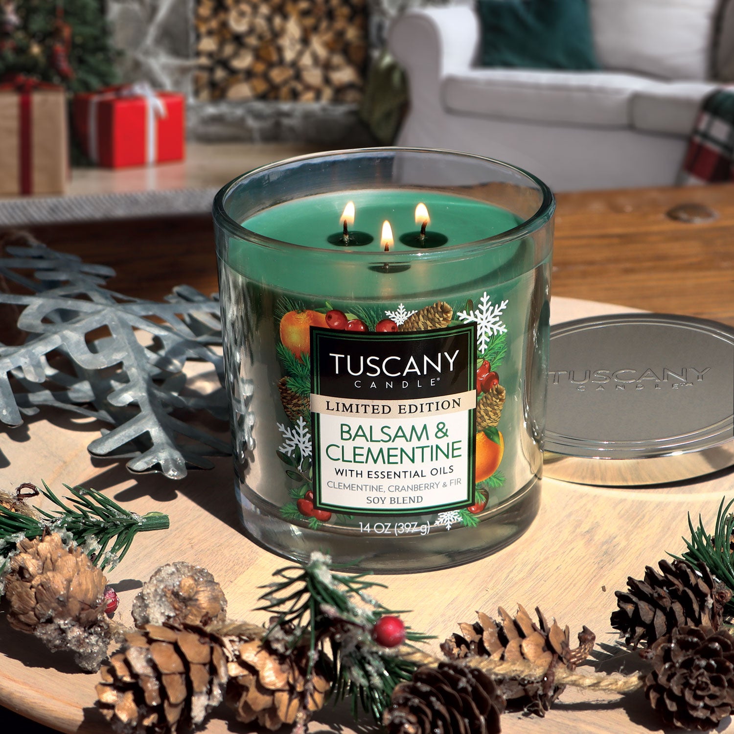A Balsam & Clementine Long-Lasting Scented Jar Candle (14 oz) by Tuscany Candle on a table next to a Christmas tree.