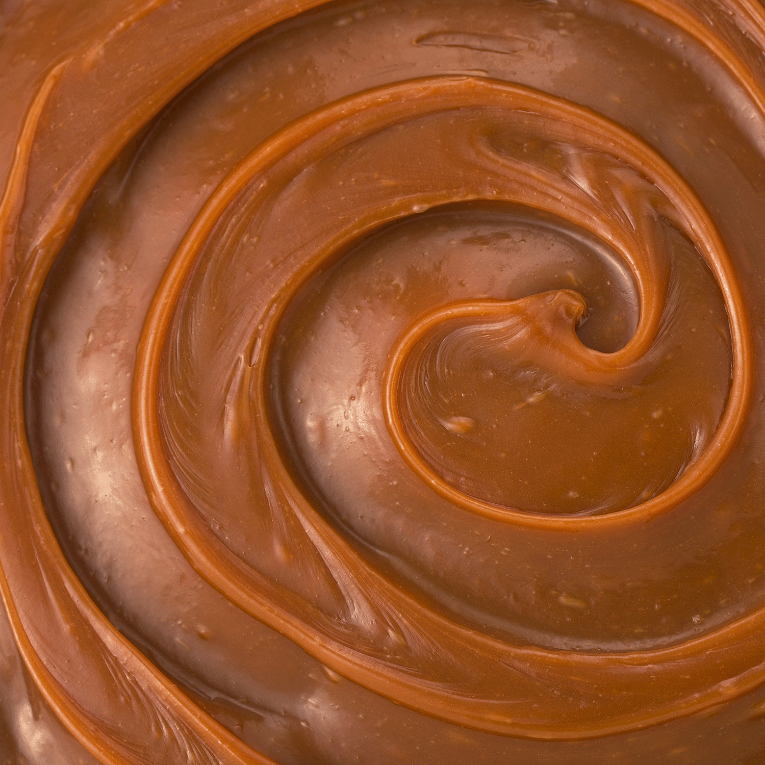 Close-up of swirled caramel highlights the rich brown hues and glossy finish of Tuscany Candle® SEASONAL Pumpkin Cheesecake: Vanilla & Roasted Cinnamon Scented Fall Candle (14 oz), made from a premium soy wax blend.
