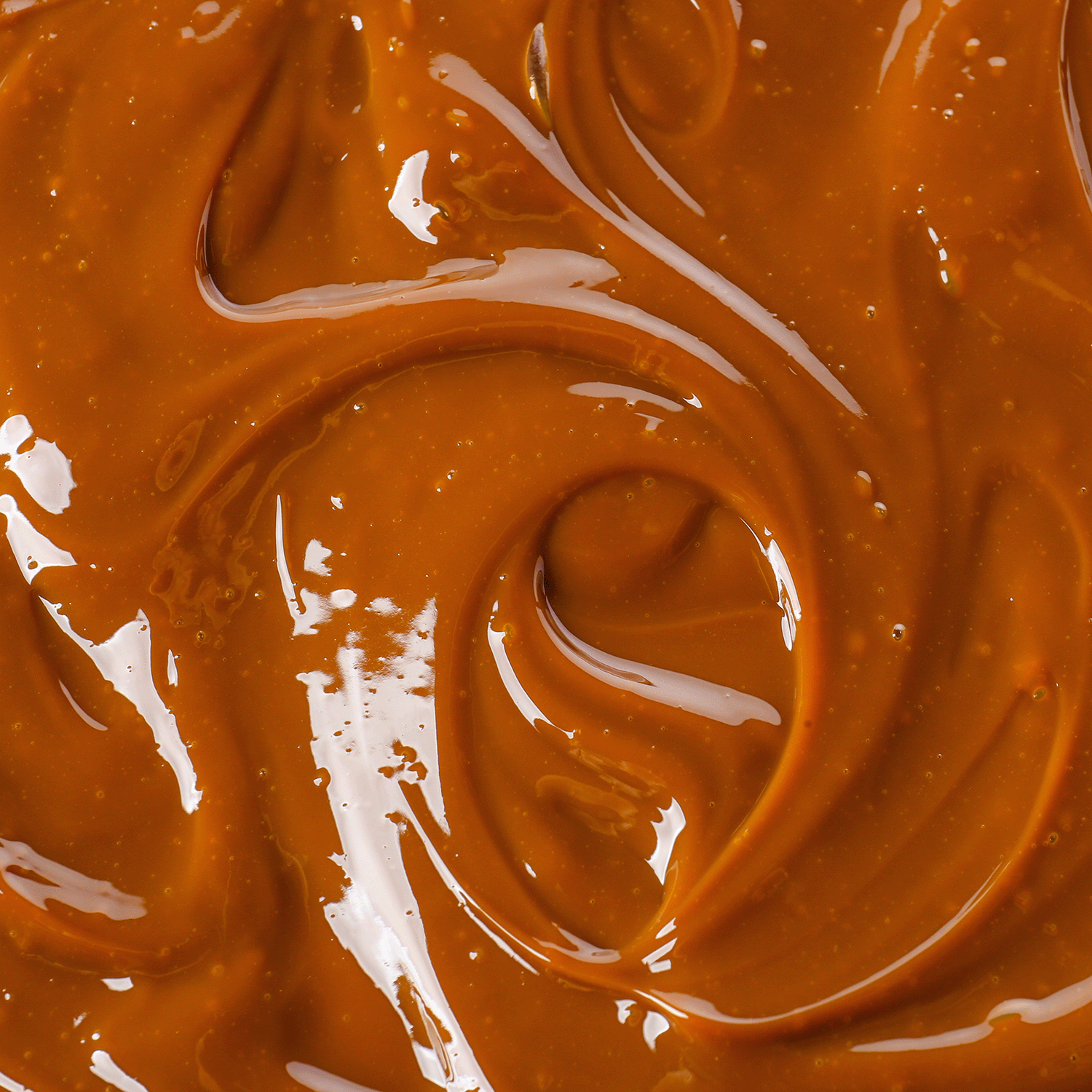 Close-up of smooth, glossy caramel swirls, evoking the rich aroma of Tuscany Candle® SEASONAL Bourbon Caramel Spice: Aged Bourbon & Vanilla Scented Fall Candle (14 oz).