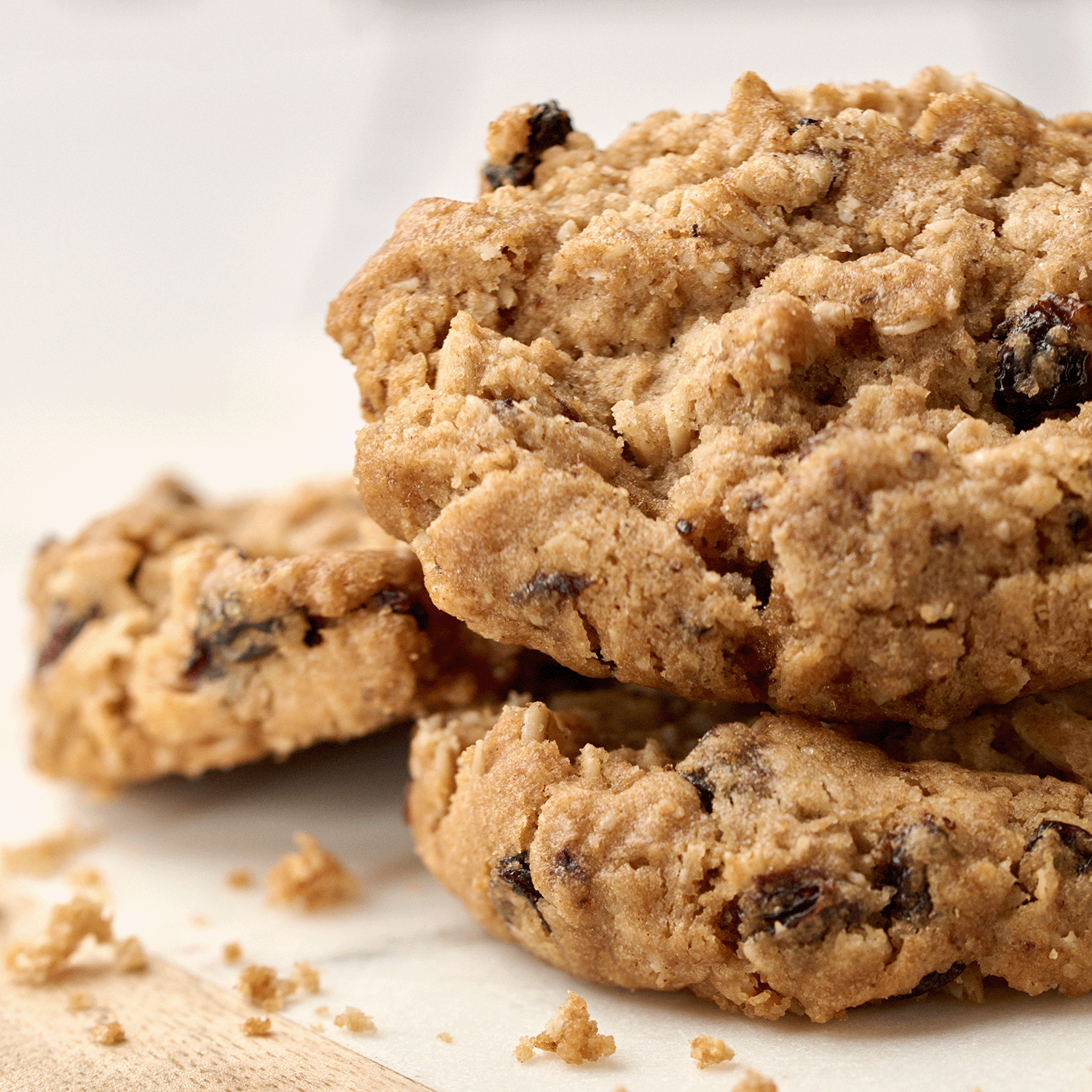 Close-up of three oatmeal raisin cookies on parchment paper—perfect for enjoying with the Tuscany Candle® SEASONAL Harvest Cookies: Brown Sugar & Vanilla Scented Fall Candle (14 oz).