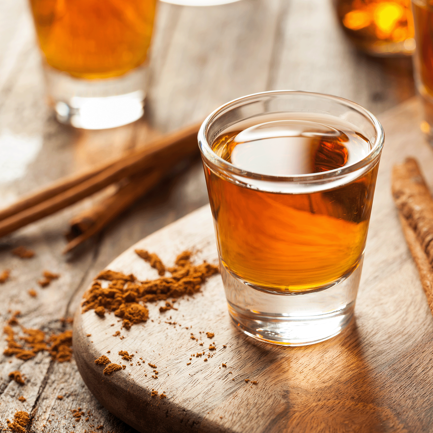 An 18 oz Tuscany Candle® SEASONAL Bourbon Caramel candle sits on a wooden board with ground cinnamon and sticks, filling the air with cozy cinnamon and maple sugar scents from its soy wax blend—perfect for fall.