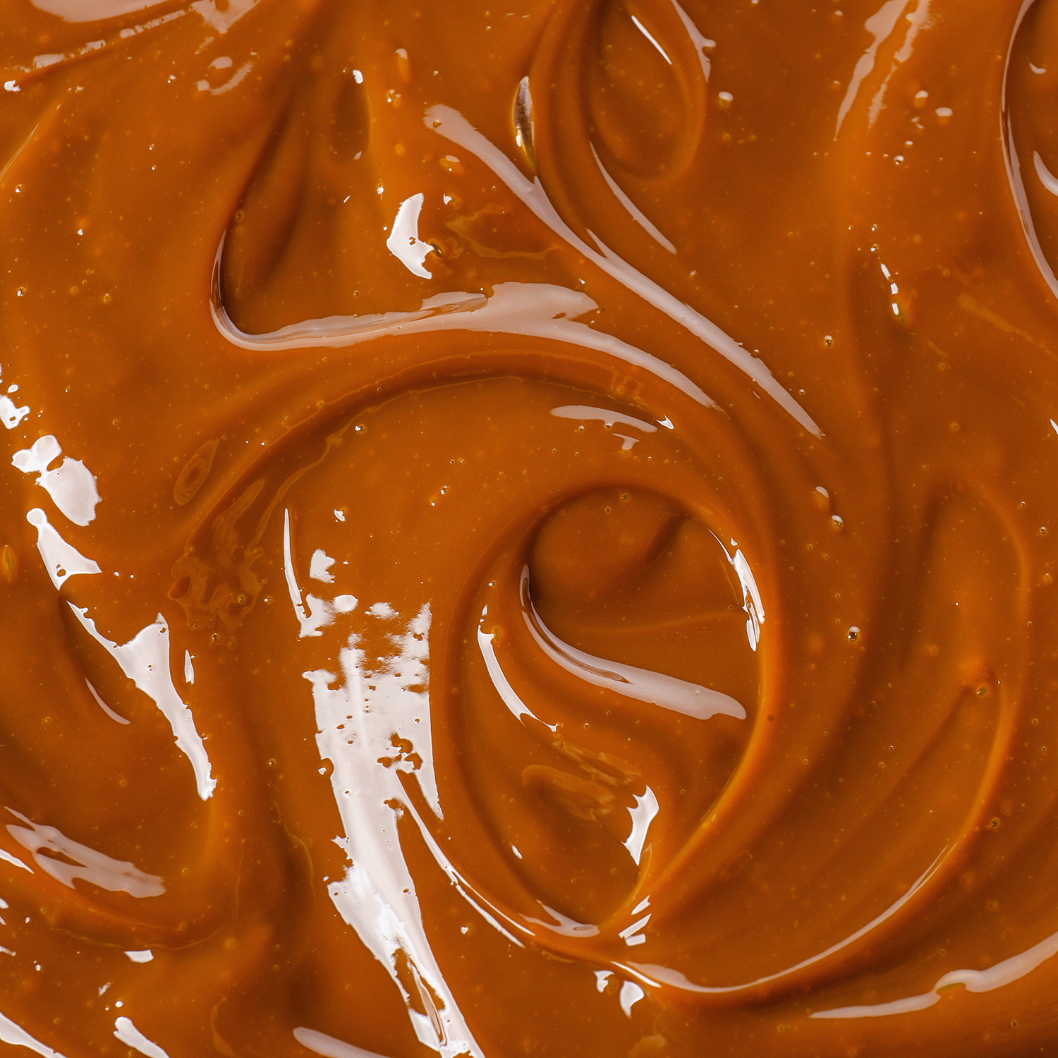 Close-up of glossy caramel sauce, inspired by the rich aroma of Bourbon Caramel: Cinnamon & Maple Sugar Scented Fall Candle (18 oz) by Tuscany Candle® SEASONAL, crafted with a premium soy wax blend.