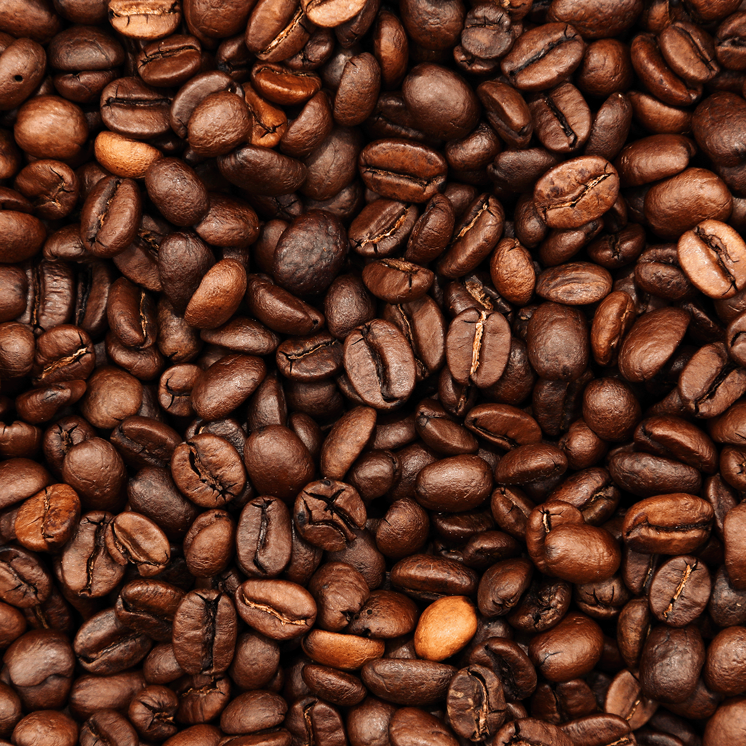 A close-up of roasted coffee beans in various brown shades and glossy surfaces, evoking the aroma of Tuscany Candle® SEASONAL Pumpkin Spice Latte: Oatmilk & Dark Roast Scented Fall Candle (12 oz).