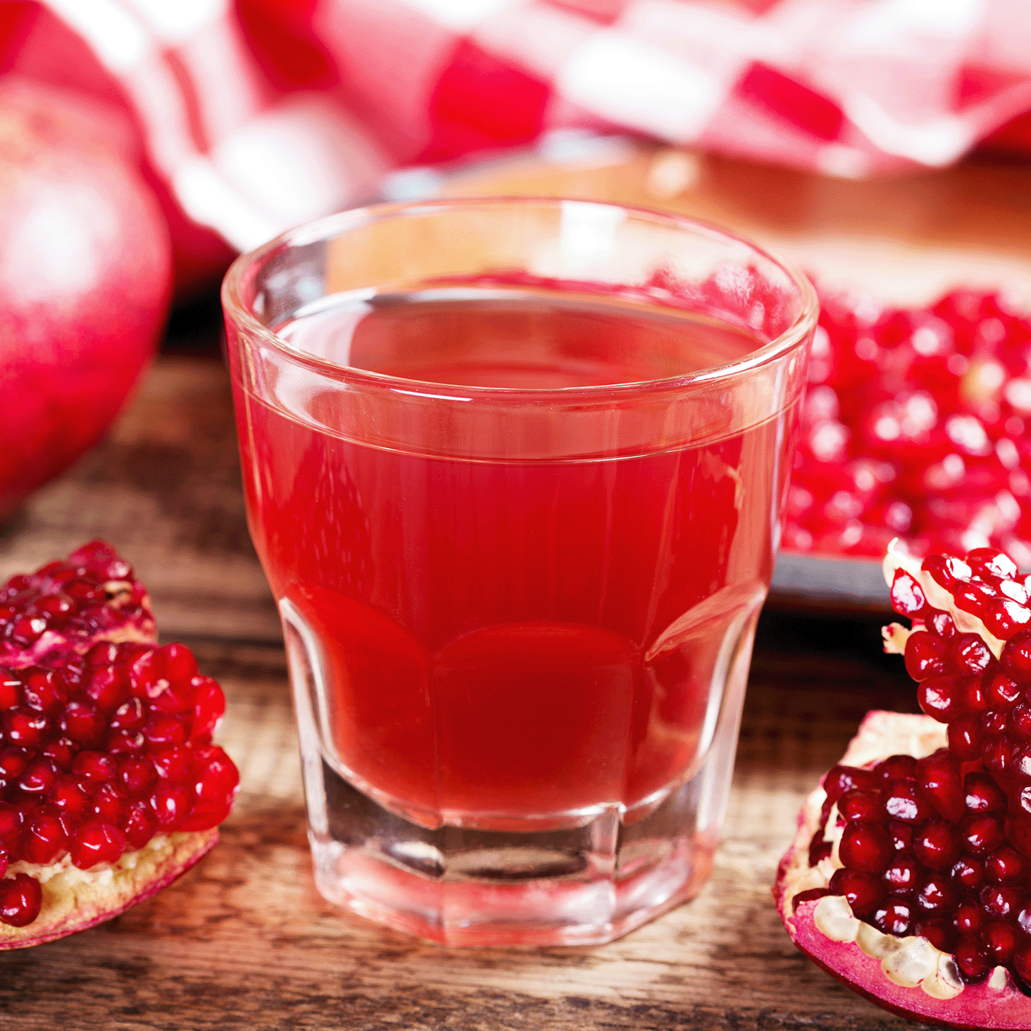 A glass of pomegranate juice on a wooden table with pomegranate halves and seeds evokes the lasting aroma of Tuscany Candle® SEASONAL Apricot & Honey: Pomegranate & Patchouli Scented Fall Wax Melt (2.5 oz).
