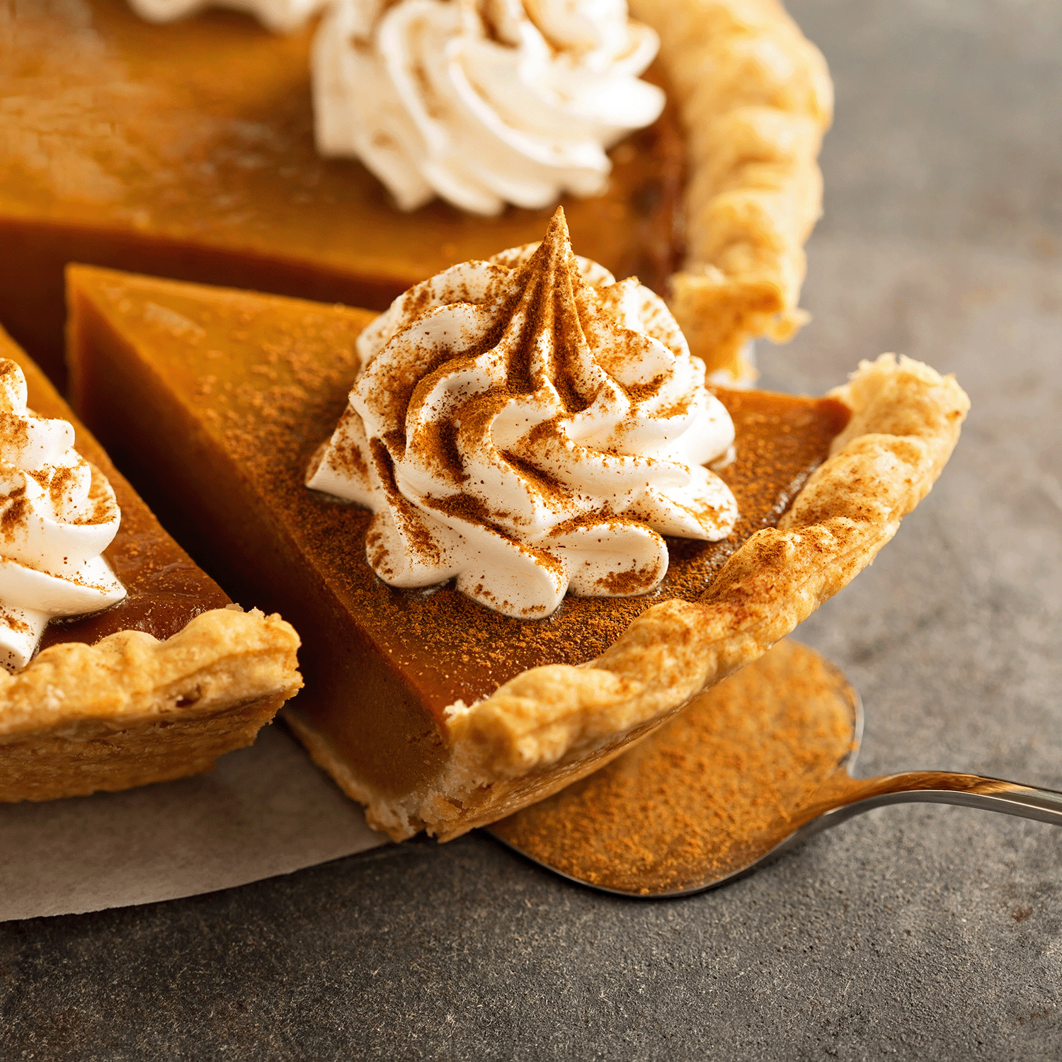 A slice of pumpkin pie with whipped cream and cinnamon evokes the cozy autumn aroma of Tuscany Candle® SEASONAL Harvest Pumpkin: Nutmeg & Clove Scented Fall Wax Melt (2.5 oz), filling the air with warm, spicy fragrance.
