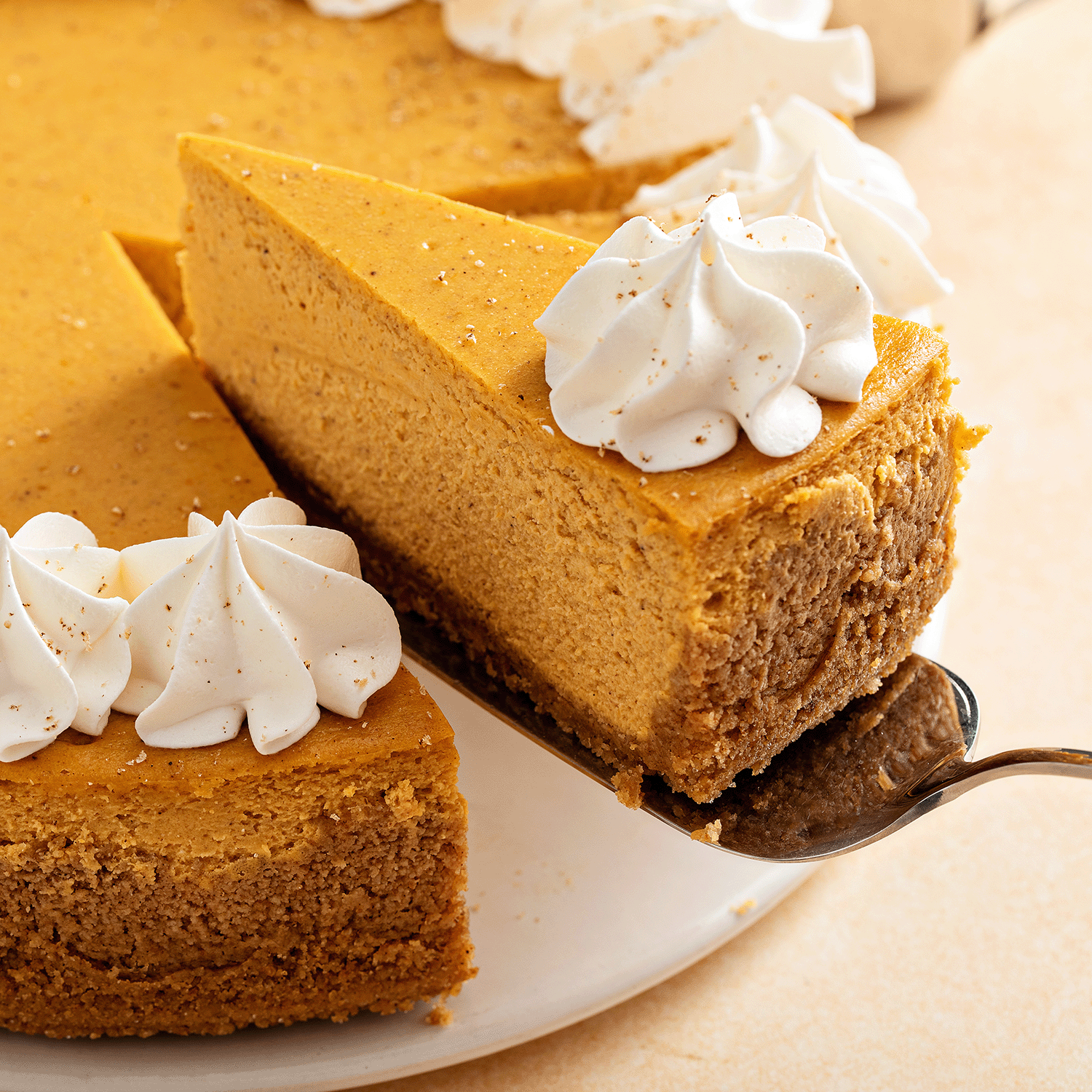 A slice of pumpkin cheesecake is lifted from a whole cake, evoking the cozy fall aroma of Tuscany Candle® SEASONAL Pumpkin Cheesecake: Vanilla & Roasted Cinnamon Scented Fall Wax Melt (2.5 oz).