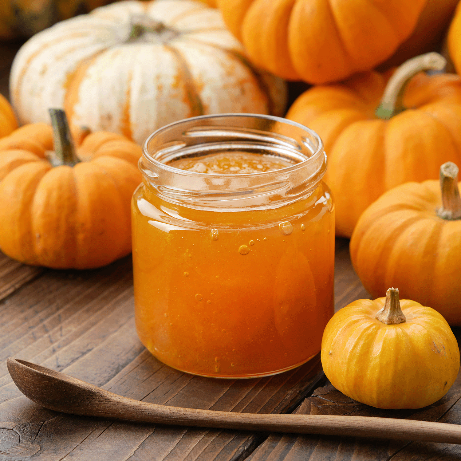 A Pumpkin Cheesecake: Vanilla & Roasted Cinnamon Scented Fall Wax Melt (2.5 oz) by Tuscany Candle® SEASONAL sits on a wooden table with pumpkins and a spoon, filling the air with cozy fall fragrance.