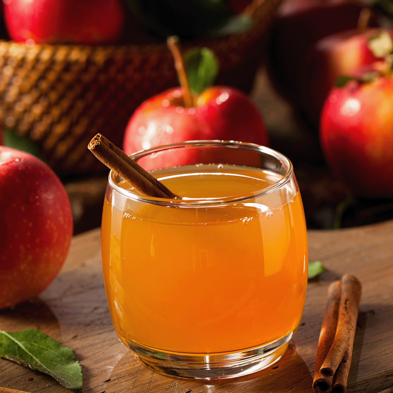 A glass of apple cider with cinnamon on wood, surrounded by red apples and spice—just like Tuscany Candle® SEASONAL Apple Cider: Sugared Ginger & Cinnamon Scented Fall Wax Melt (2.5 oz), crafted from a natural soy blend for the perfect autumn aroma.
