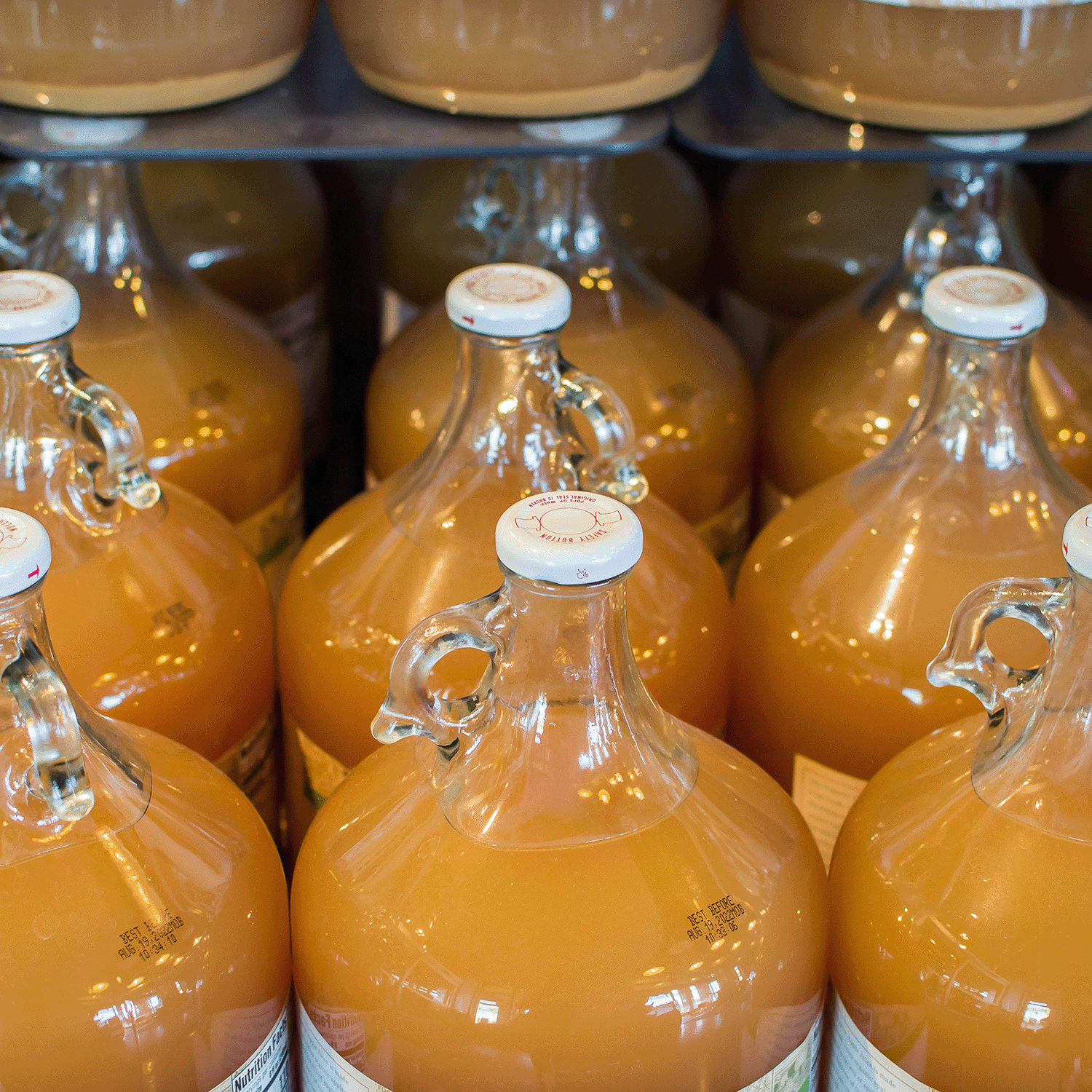 Several 14 oz Autumn Bliss: Apple Cider & Clove scented candles from Tuscany Candle® SEASONAL, with a warm orange-brown hue, are arranged closely on a shelf, evoking cozy fall vibes.