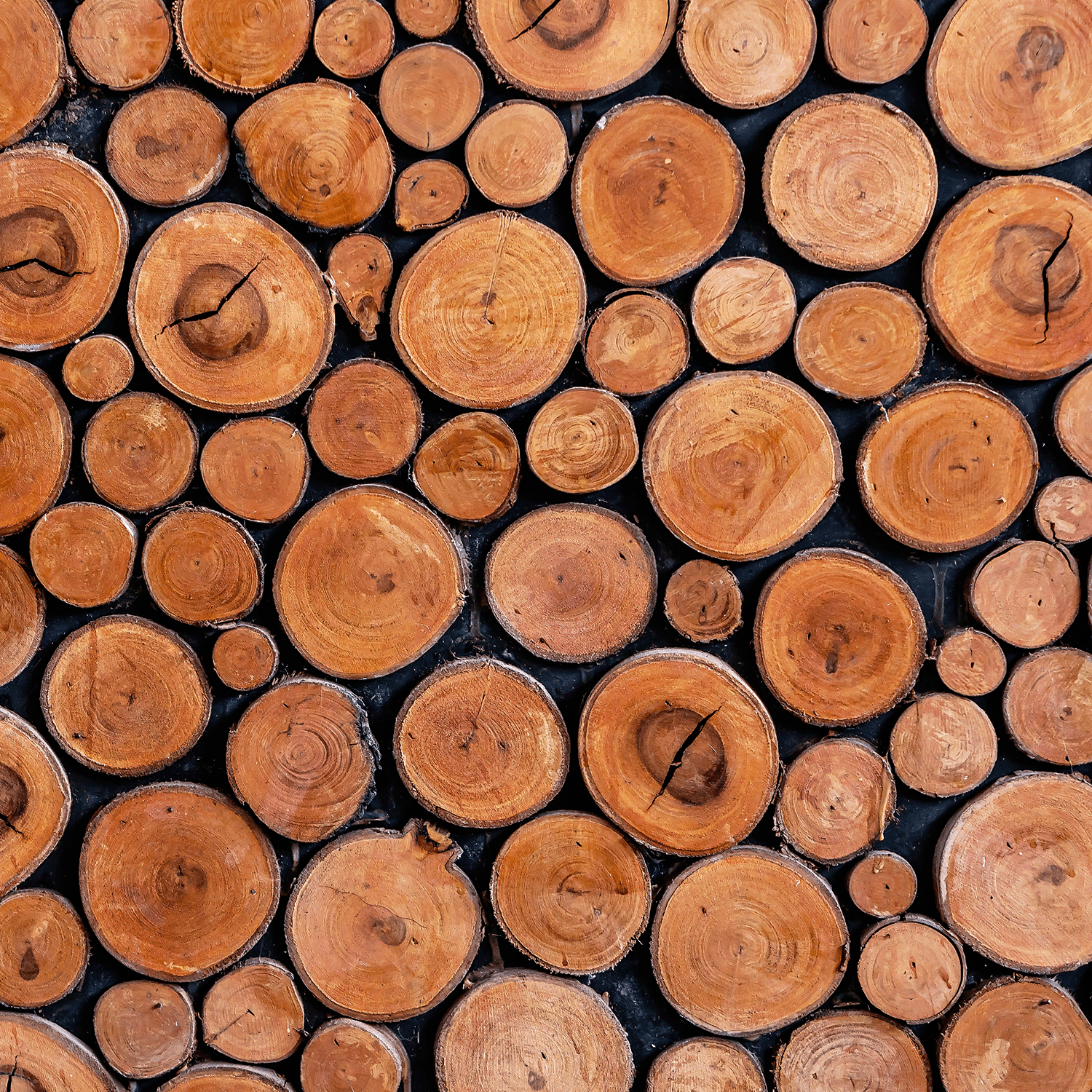 Close-up of stacked wooden logs with natural grain against a dark background—an inviting image that inspires the Autumn Dreams: Black Cherry & Amber Oud Scented Fall Candle (14 oz) by Tuscany Candle® SEASONAL from the Simply Fall Collection.