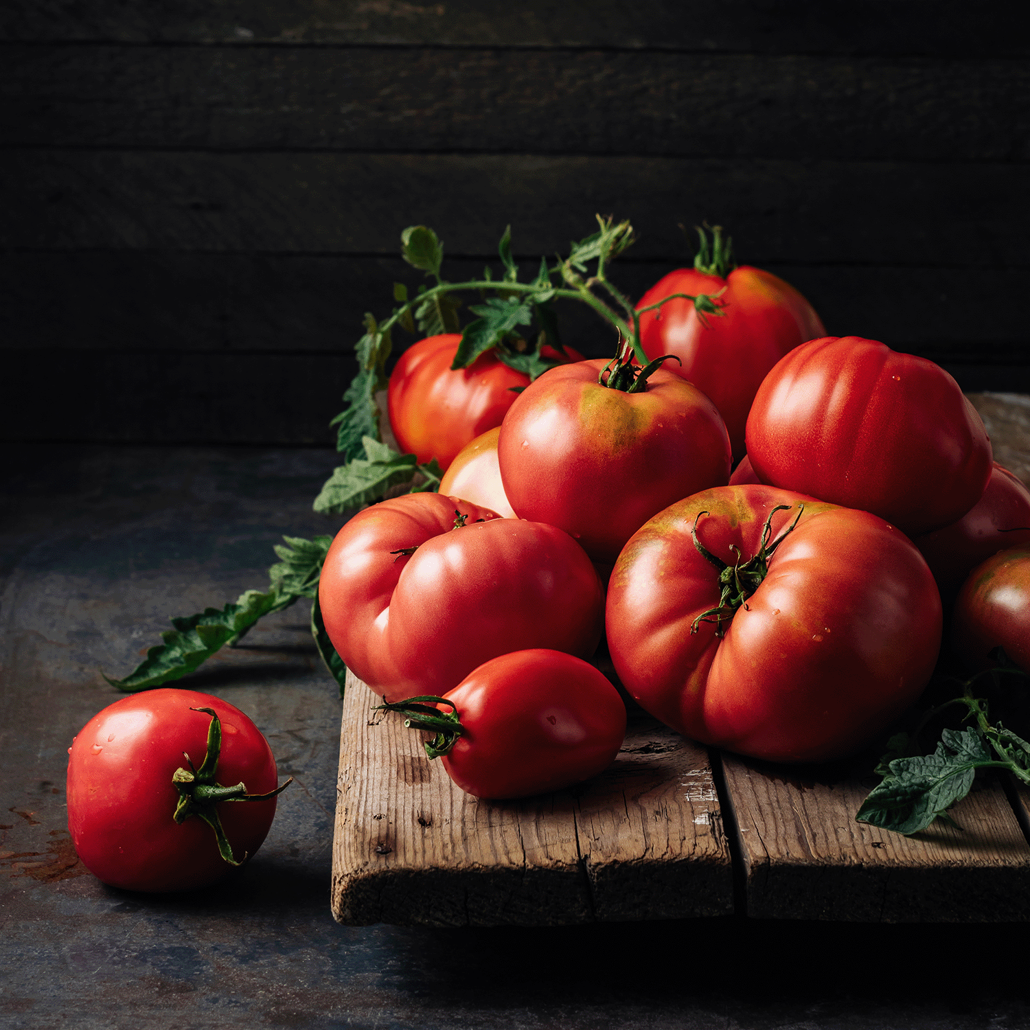 A cluster of ripe red tomatoes with green stems rests on wood, capturing the fresh scent of Tuscany Candle® SEASONAL's Ghostly Garden: Tomato Vine & Moss Scented Halloween Candle (14 oz).
