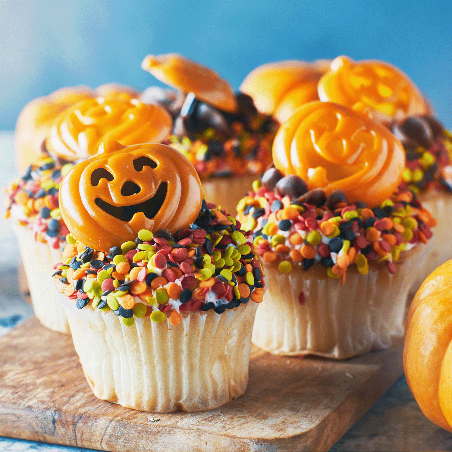 Vanilla cupcakes with orange jack-o’-lantern candies and sprinkles evoke the scent of Tuscany Candle® SEASONAL’s Charmed Sweets: Vanilla Cupcake & Buttercream Icing Scented Halloween Candle (14 oz).
