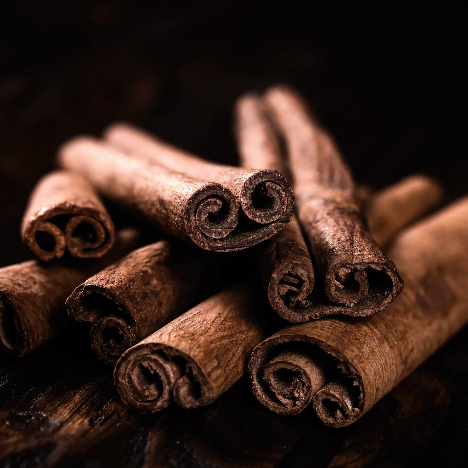 Cinnamon sticks rest on dark wood, inspiring the warm, spicy aroma of Tuscany Candle® SEASONAL's Grizzly Ghouls: Autumnal Spices & Fogged Musk Scented Halloween Wax Melt (2.5 oz)—the perfect fall fragrance.