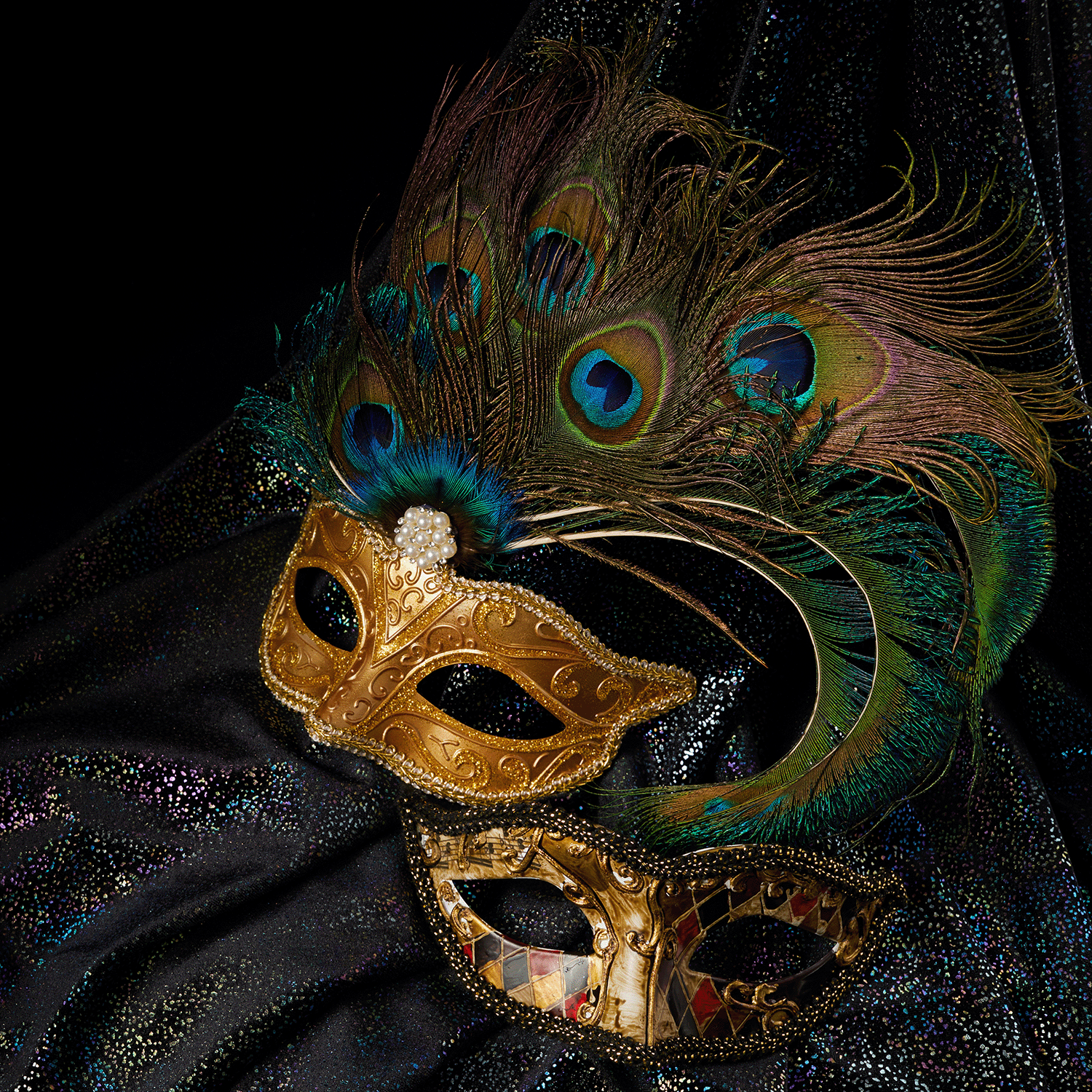 Two ornate masquerade masks—one gold with peacock feathers, the other with a harlequin pattern—adorn a dark backdrop, setting the scene for enjoying Tuscany Candle® SEASONAL's Masquerade Party: Blackberry & Birch Bark wax melt.