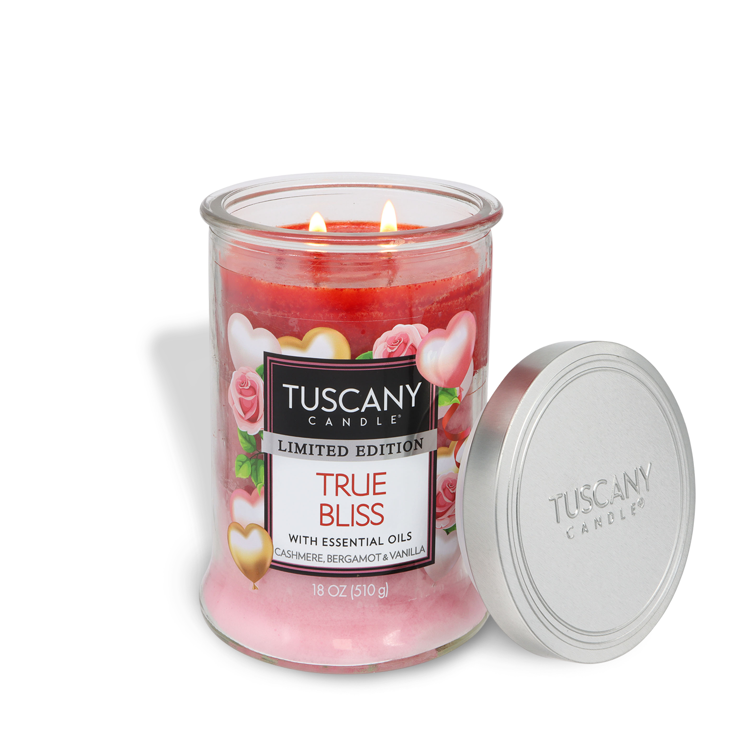An 18 oz glass jar of Tuscany Candle® SEASONAL's True Bliss: Cashmere & Vanilla Scented Valentine's Candle with pink wax, two lit wicks, rose decor, and a silver lid beside it. The scent blends cashmere, bergamot, and vanilla.