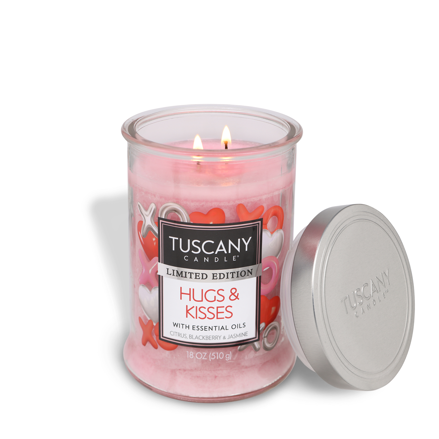 A pink 18 oz Tuscany Candle® SEASONAL "Hugs & Kisses: Lemon & Jasmine Scented Valentine's Candle" with two lit wicks, XOXO and heart design, sits beside its silver lid.