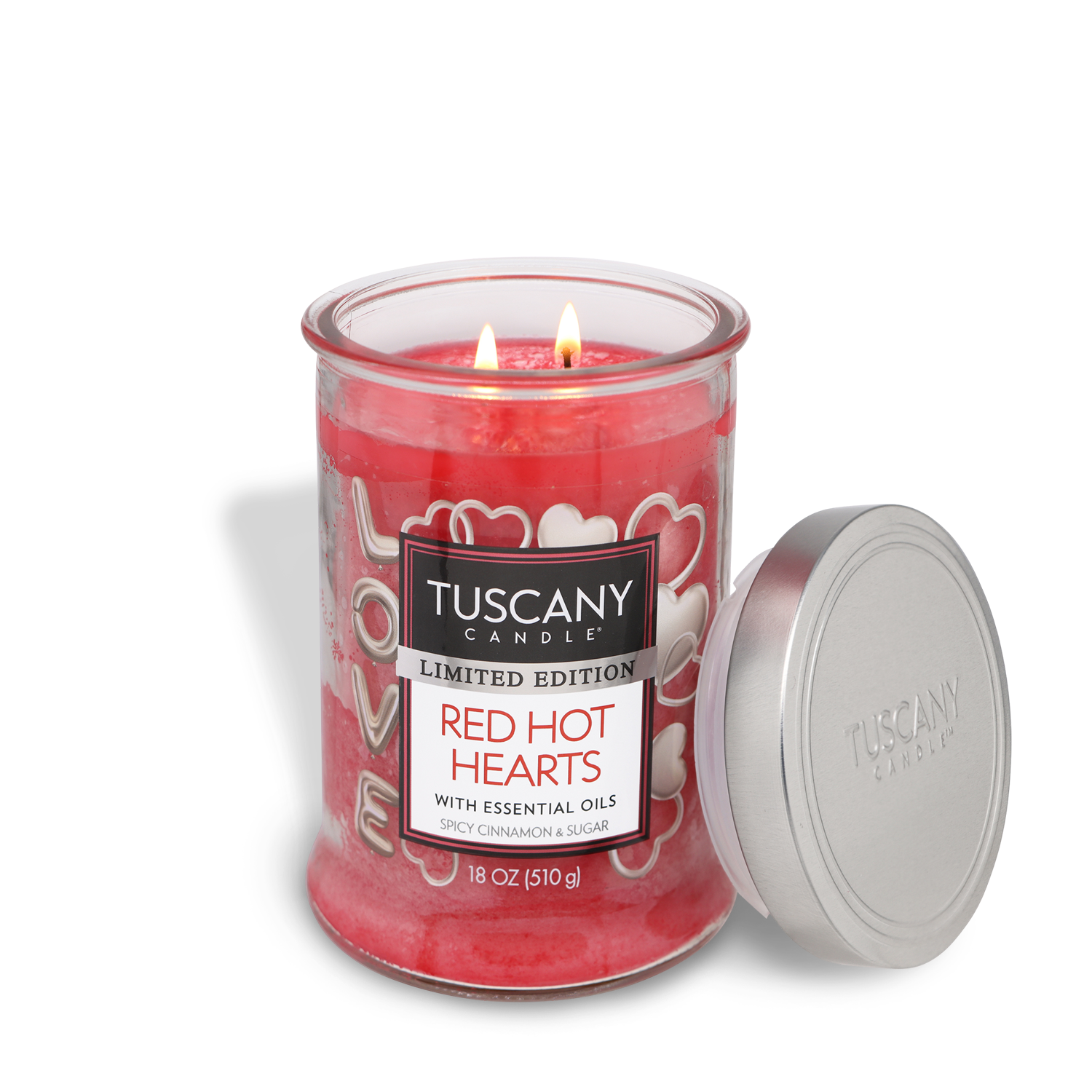 A lit Tuscany Candle® SEASONAL "Red Hot Hearts: Red Hot Cinnamon Scented Valentine's Candle" (18 oz) with essential oils sits beside its silver lid. The red glass jar features white hearts and "LOVE.