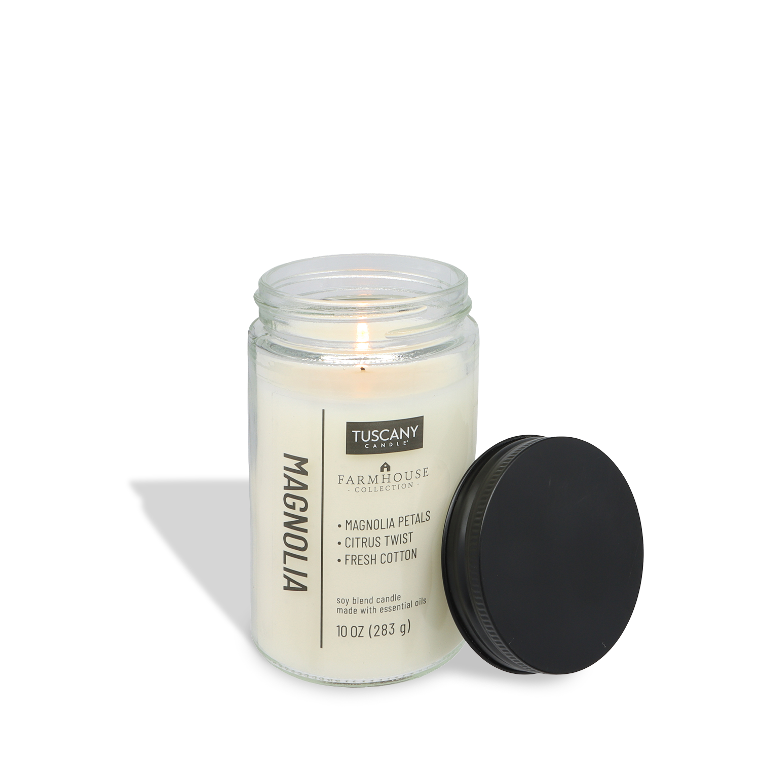 A lit Tuscany Candle® EVD Magnolia Scented Jar Candle (10 oz) from the Farmhouse Collection sits in a clear glass jar with a black lid. Magnolia petals, citrus twist, and fresh cotton create the perfect cozy soy blend fragrance.