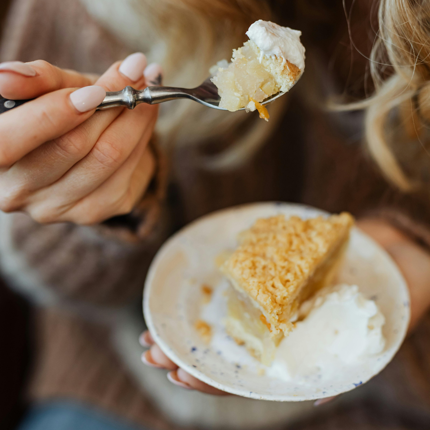 A person lifts a forkful of pie with whipped cream as the warm glow of a Tuscany Candle® EVD Comforts of Home Scented Jar Candle (10 oz) from the Farmhouse Collection flickers in a mason jar nearby.