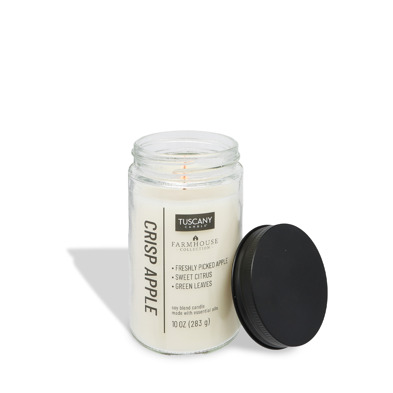 A lit Tuscany Candle® EVD Crisp Apple Scented Jar Candle (10 oz) from the Farmhouse Collection with a black lid sits nearby; its label highlights apple, citrus, and green leaves fragrances.