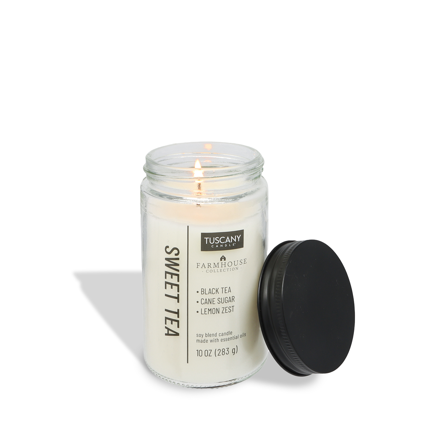 A lit Tuscany Candle® EVD Sweet Tea Scented Jar Candle (10 oz) from the Farmhouse Collection, with a black lid beside it, fills your space with a warm, inviting aroma.