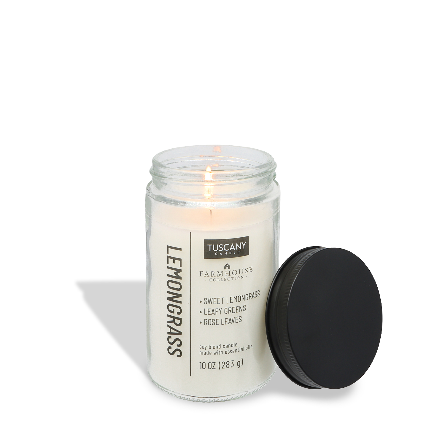 A lit Tuscany Candle® EVD Lemongrass Scented Jar Candle (10 oz) – Farmhouse Collection sits in its glass jar, with the black lid resting on its side.