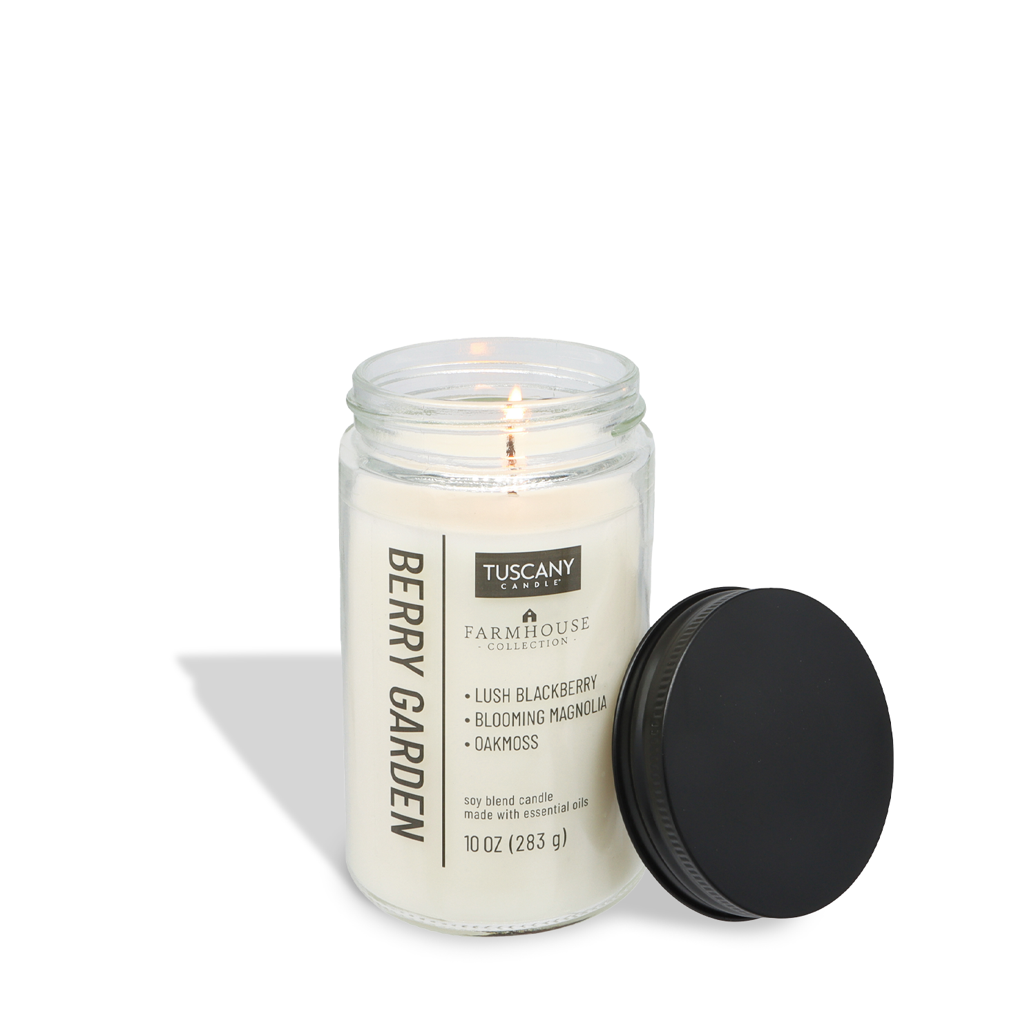 A lit Tuscany Candle® EVD Berry Garden Scented Jar Candle (10 oz) from the Farmhouse Collection sits in a clear glass jar, "Berry Garden" label visible, with its black lid set aside—perfect for farmhouse décor.