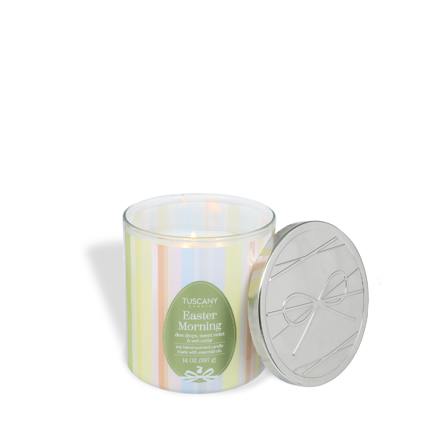 A Tuscany Candle® Easter Morning: Dew Drops & Violet Scented Spring Candle (14 oz) is lit with its silver lid beside it on a white surface.