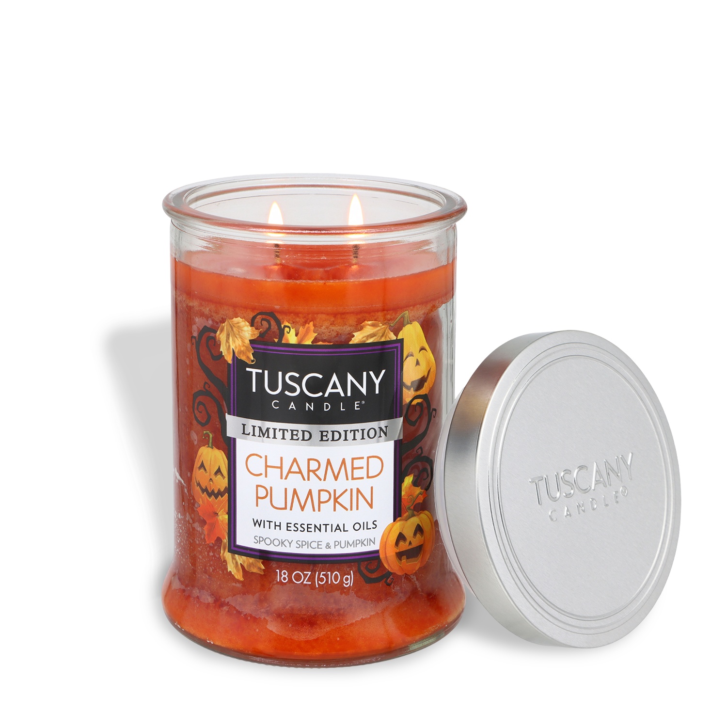 A Tuscany Candle® SEASONAL “Charmed Pumpkin: Spooky Spice & Pumpkin Scented Halloween Candle” (18 oz) jar with autumn and Halloween decorations, two lit wicks, and a silver lid placed beside it.