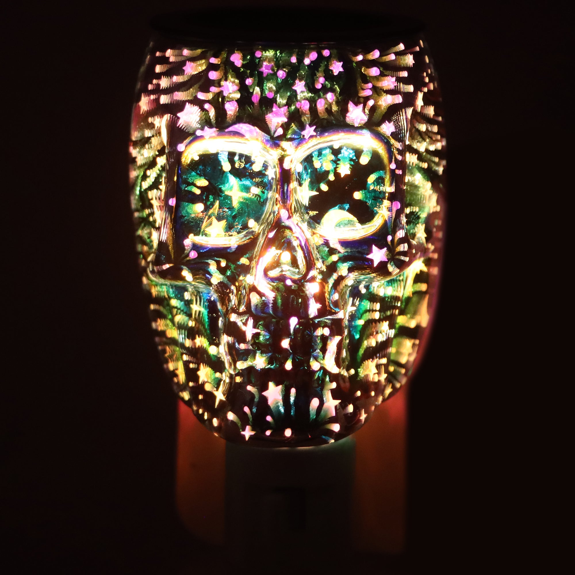 The Tuscany Candle® SEASONAL Holographic Skull Outlet Wax Melt Warmer casts colorful lights and shimmering star patterns against a dark backdrop.