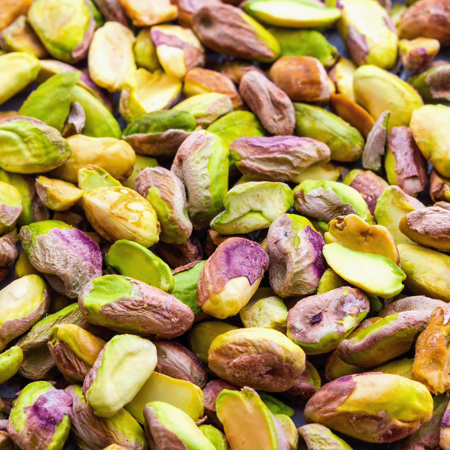 Close-up of shelled pistachio nuts reveals vibrant green, yellow, and purple hues—perfect inspiration for the Tuscany Candle® SEASONAL Glazed Croissant: Butter & Pistachio Scented Fall Candle (14 oz), a bakery-inspired autumn fragrance that captures the cozy essence of fall.