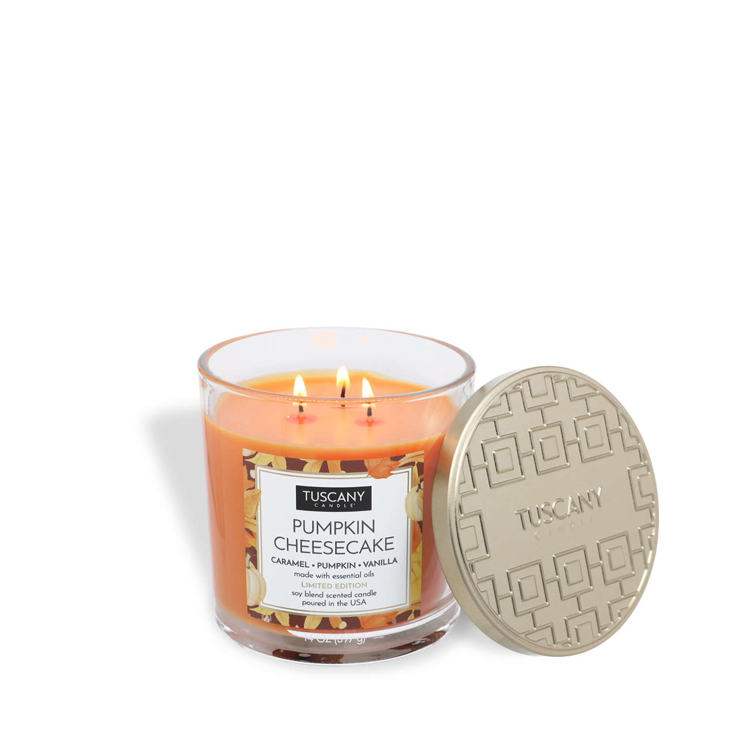 A 14 oz Tuscany Candle® SEASONAL glass jar candle labeled "Pumpkin Cheesecake: Caramel & Vanilla Scented Fall Candle" with three lit wicks sits beside its gold-patterned lid.