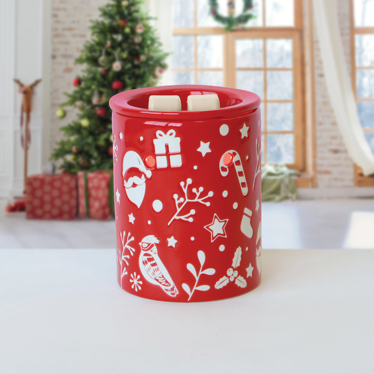 Tuscany Candle® SEASONAL Morning Snowfall: Eucalyptus & Winter Woods Scented Holiday Wax Melt (2.5 oz) in a red wax warmer with white icons and two wax cubes, on a white surface before a blurred tree.