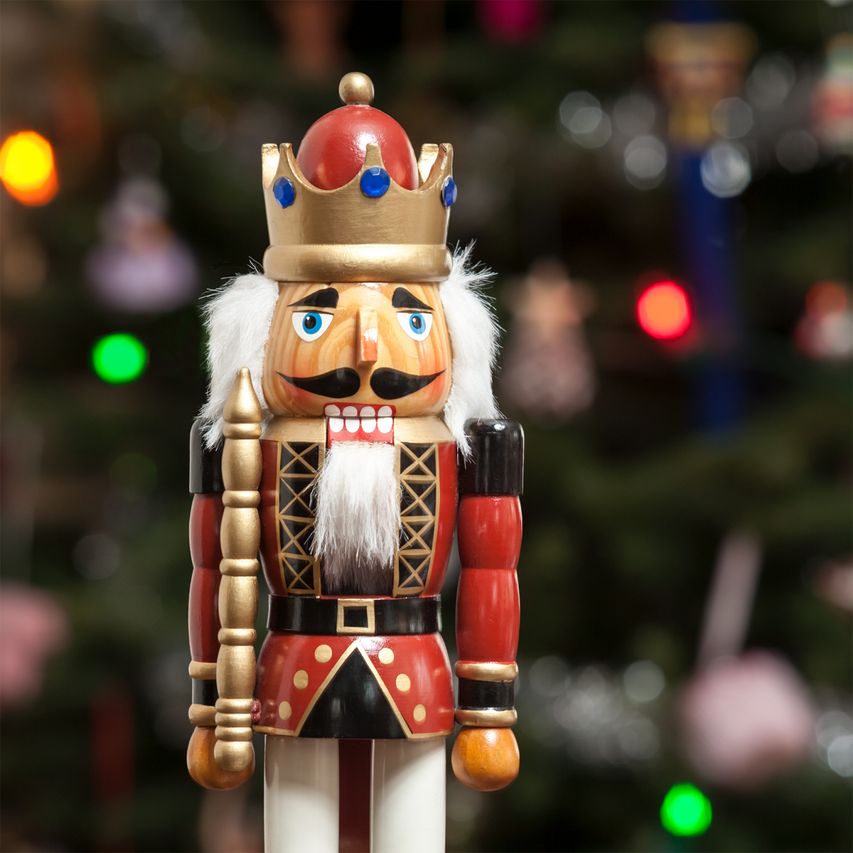 A Nutcracker Nights: Acorn & Hazelnut Scented Holiday Wax Melt (2.5 oz) featuring a nutcracker in a crown and red uniform, set against a blurred background of a lit Christmas tree.