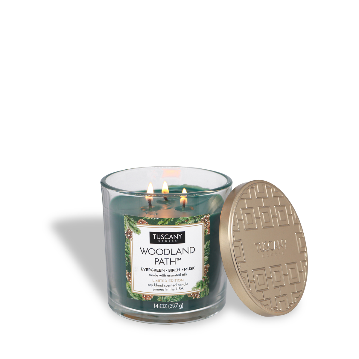 A lit, dark green Woodland Path®: Evergreen & Birch Scented Holiday Candle (14 oz) in a glass jar with its gold, patterned lid resting beside it.