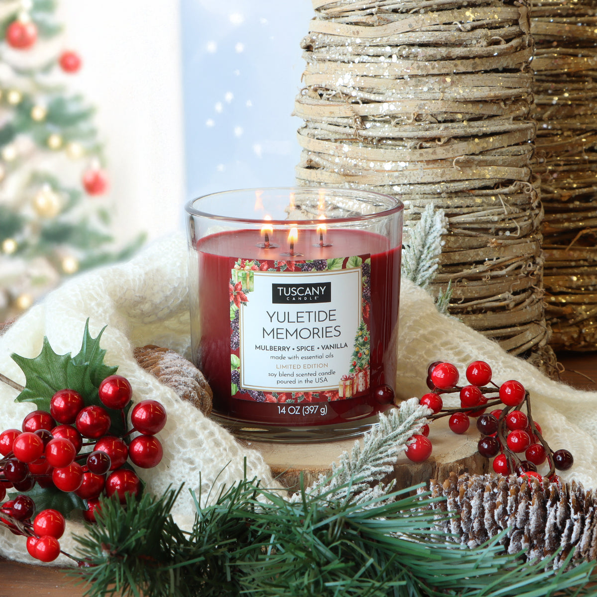 A Tuscany Candle® SEASONAL Yuletide Memories: Mulberry & Spice Scented Holiday Candle (14 oz) in a glass jar, surrounded by holly berries, pine branches, a pinecone, and a white knitted throw.