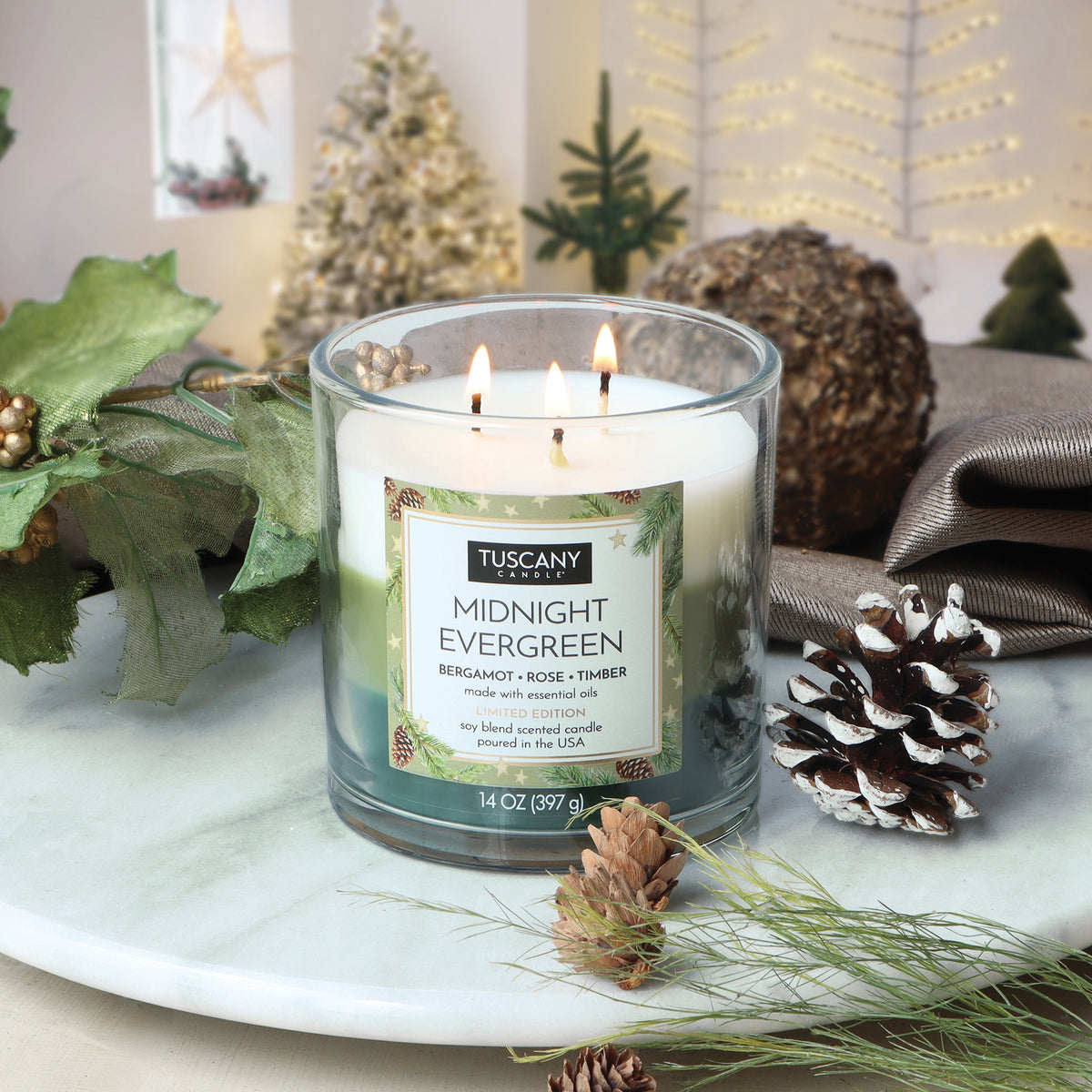Midnight Evergreen: Bergamot & Rose Scented Holiday Candle (14 oz) in a clear three-wick glass jar with layered green wax, decorated with pinecones and greenery.