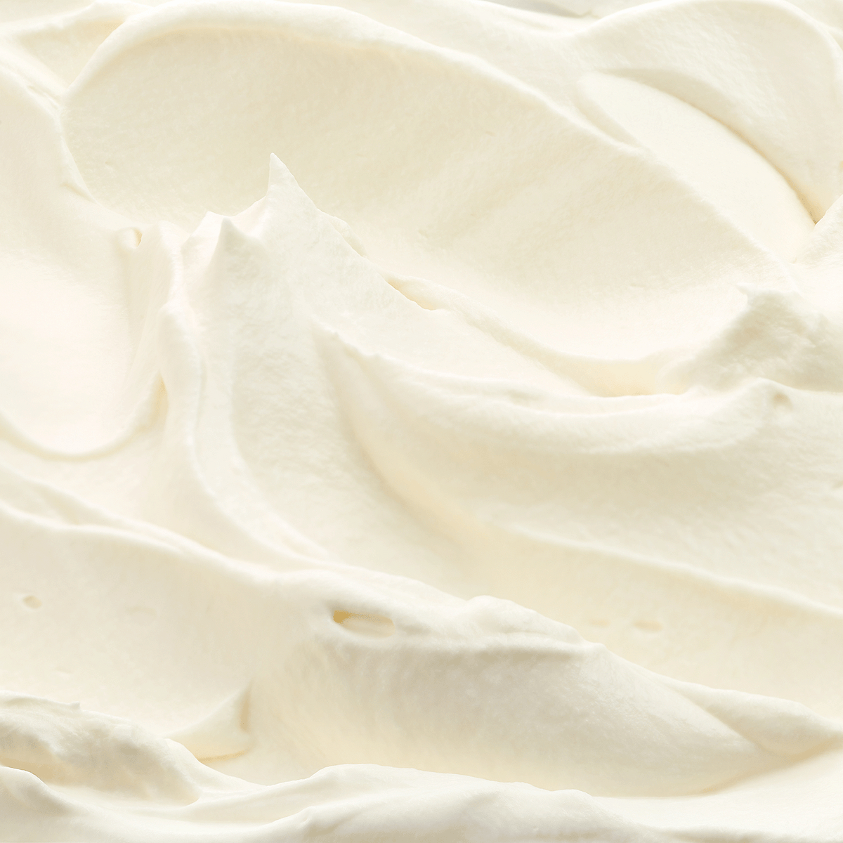 Close-up of thick, creamy white frosting with textured swirls on a Santa’s Bakeshop: Almond & Vanilla Scented Holiday Candle (18 oz).