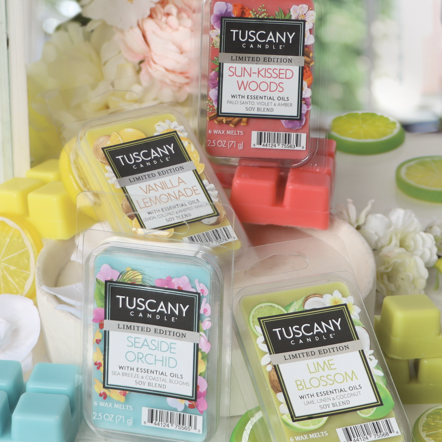 Displayed are four Tuscany Candle wax melt packages: Sun-Kissed Woods, Vanilla Lemonade, Lime Blossom, and Seaside Orchid from the Tuscany Candle® SEASONAL collection. Decorative fruits and flowers grace the background.