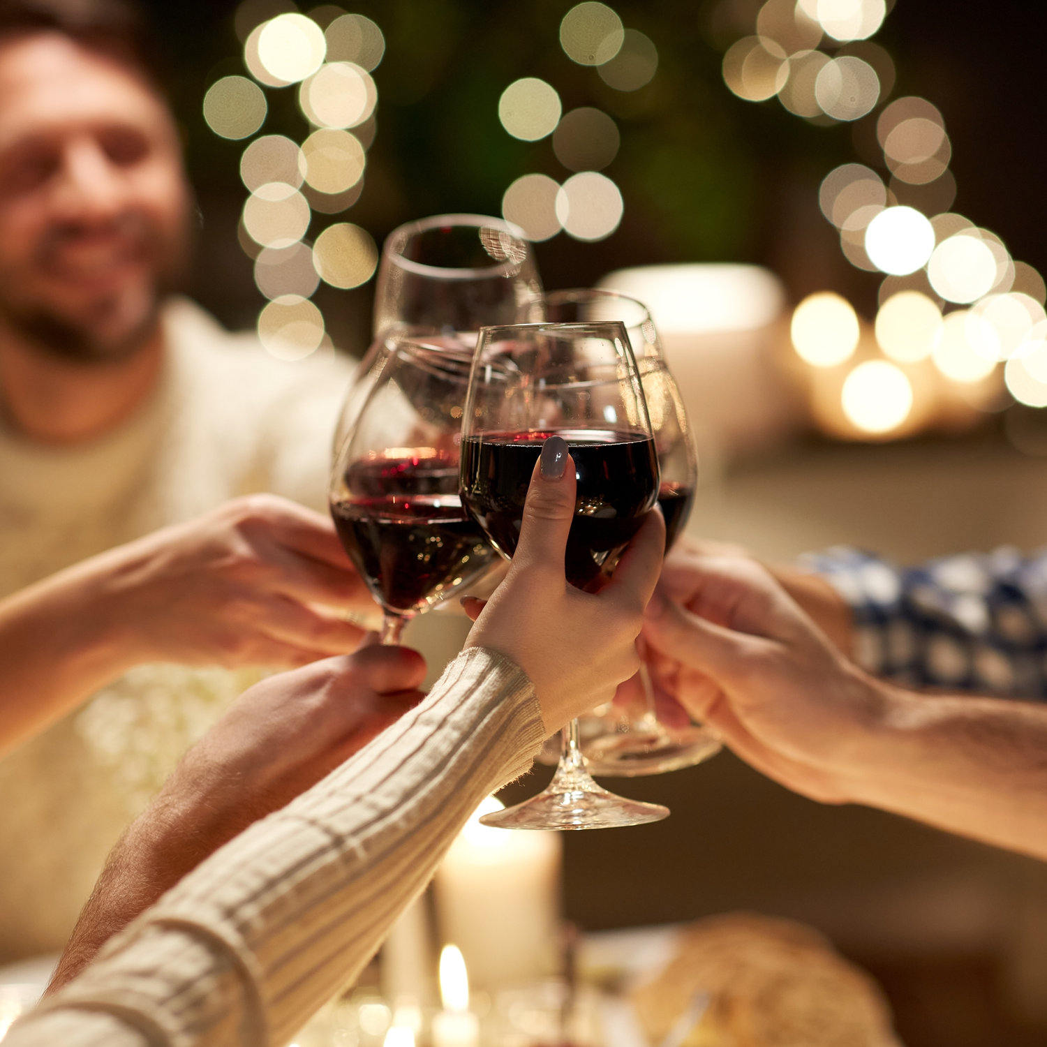 A group of people toasting Cheers Scented Candle (14 oz) – Celebrations Collection wine glasses at a dinner table during a holiday celebration.