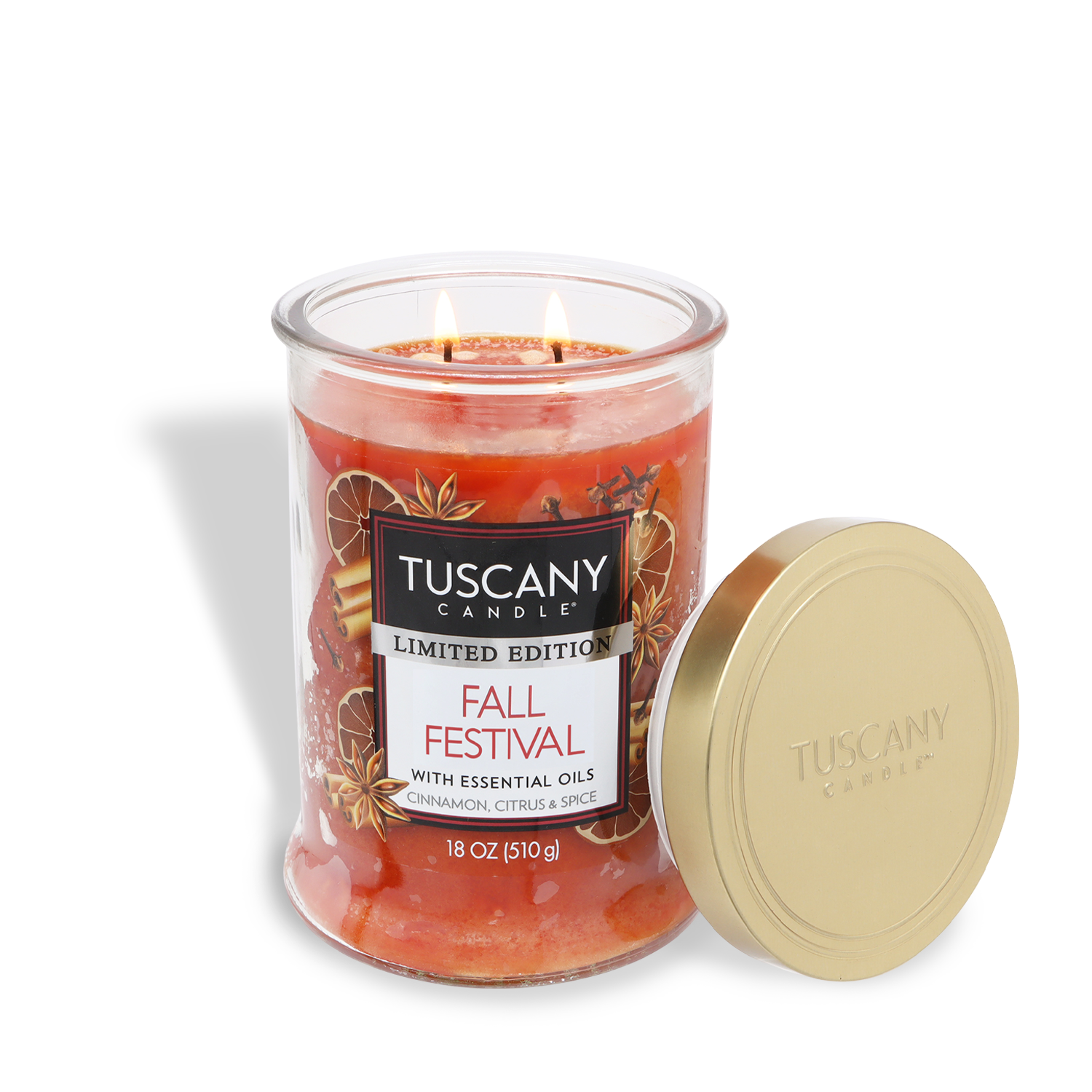 A Tuscany Candle® SEASONAL "Fall Festival: Cinnamon & Clove" 18 oz limited edition jar with gold lid sits lit; its label highlights cinnamon, citrus, and spice scents.