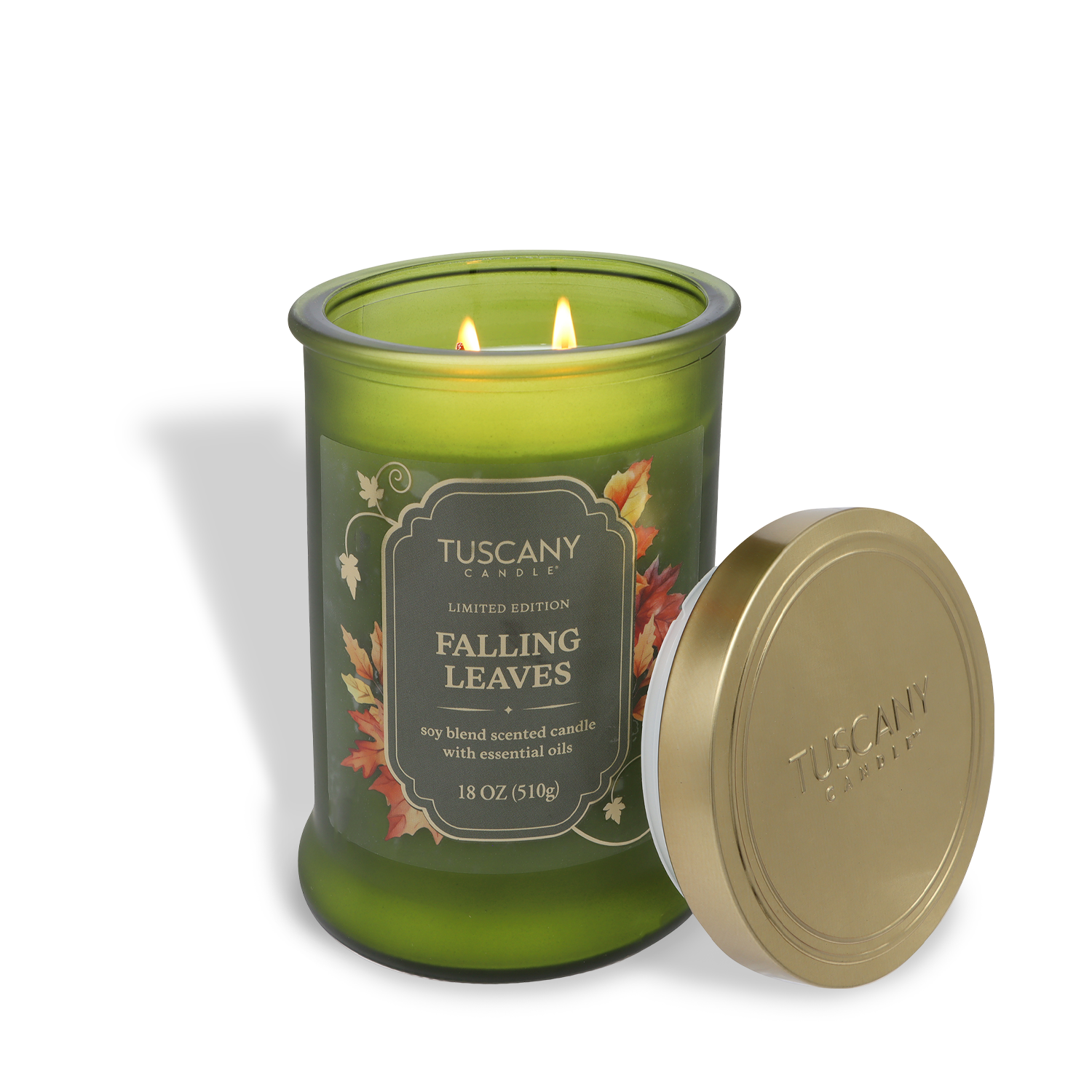 An 18 oz Tuscany Candle® SEASONAL jar, labeled “Falling Leaves: Warm Applewood & Amber,” features two lit wicks; its gold lid, set on its side, displays the brand name.