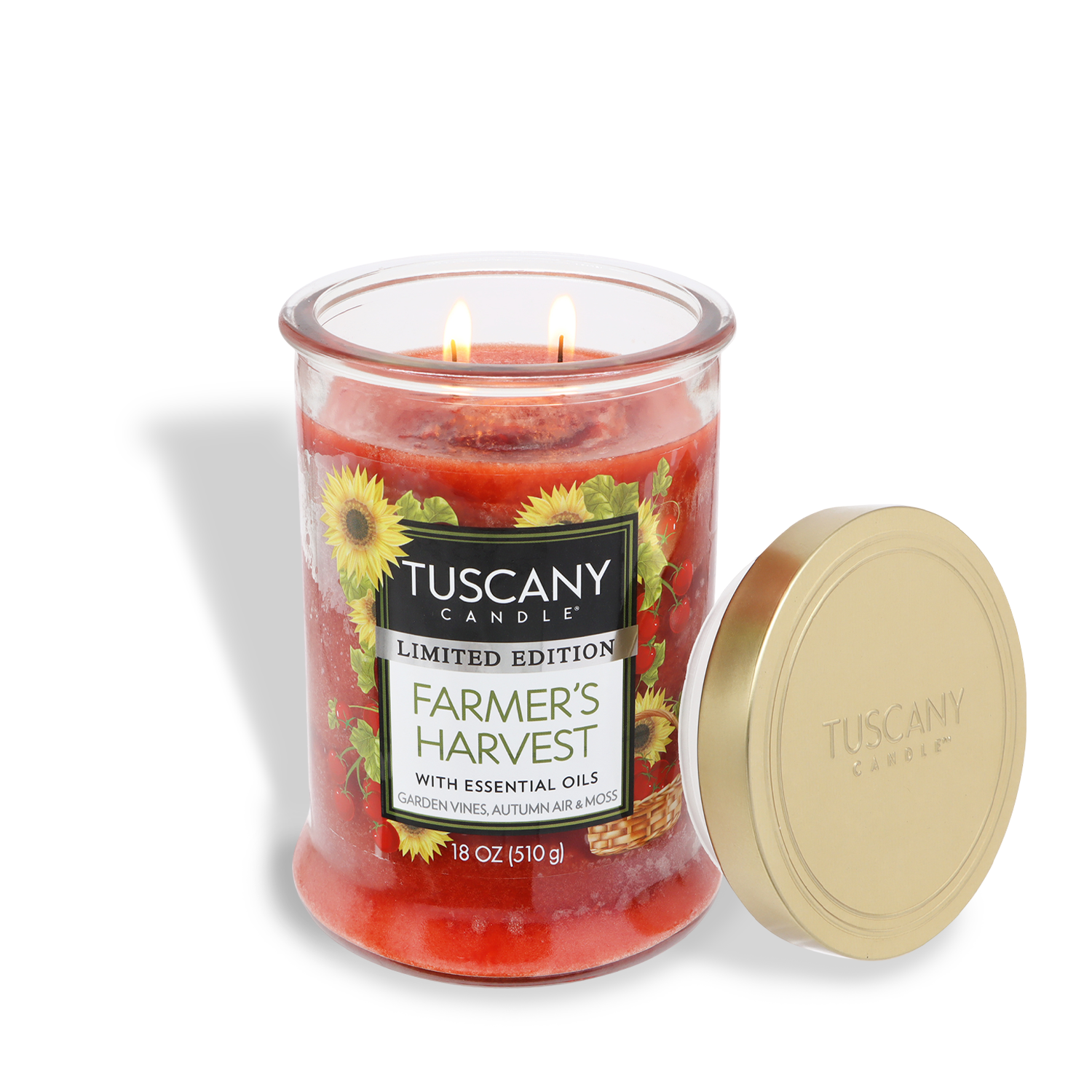 An 18 oz Tuscany Candle® SEASONAL "Farmer's Harvest: Garden Vine & Geranium" fall candle with two wicks lit, sunflowers on the label, and a gold lid beside it.