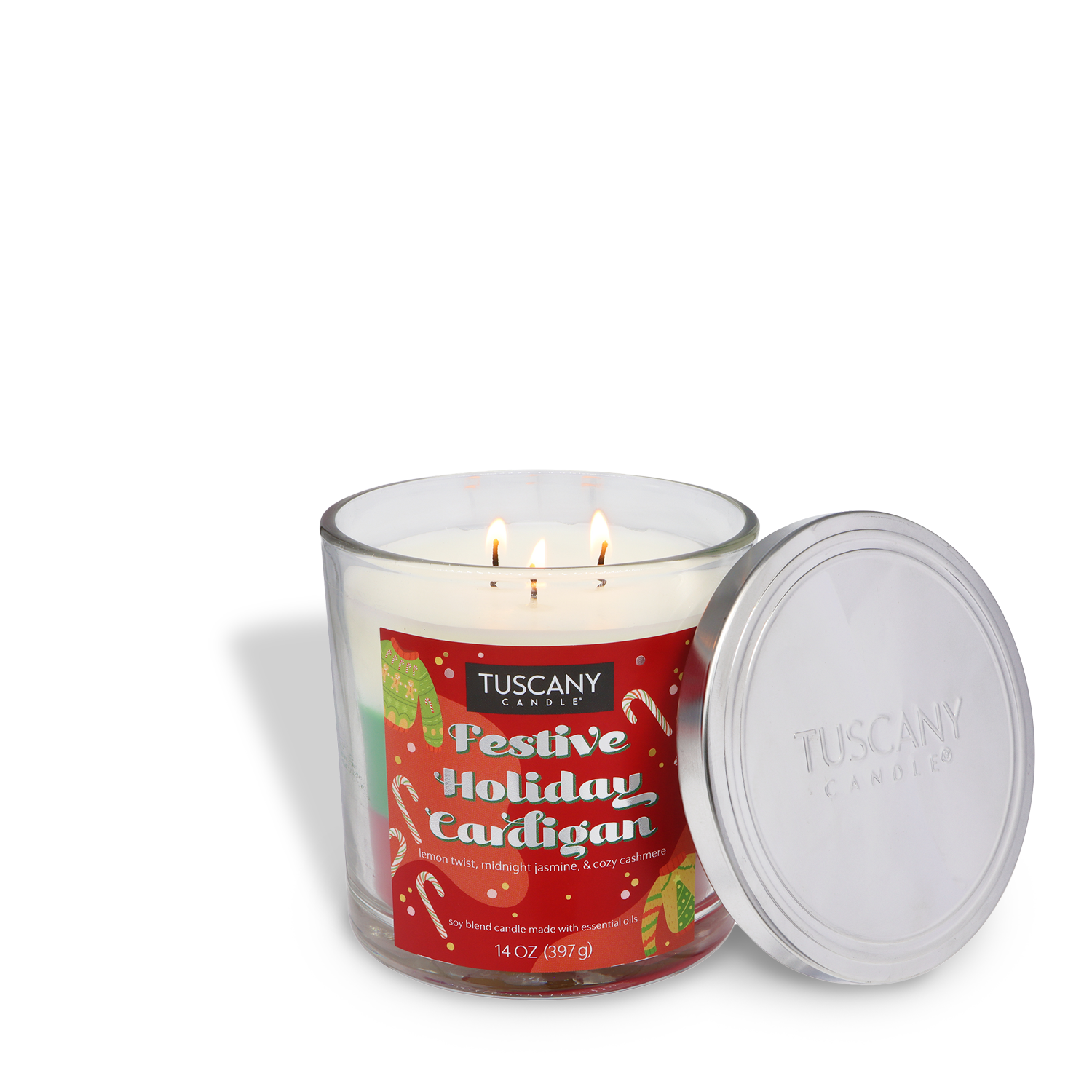 A lit Tuscany Candle® SEASONAL "Festive Holiday Cardigan Scented Holiday Candle" (14 oz) in a clear glass jar with a holiday-themed label and a silver lid placed beside it.