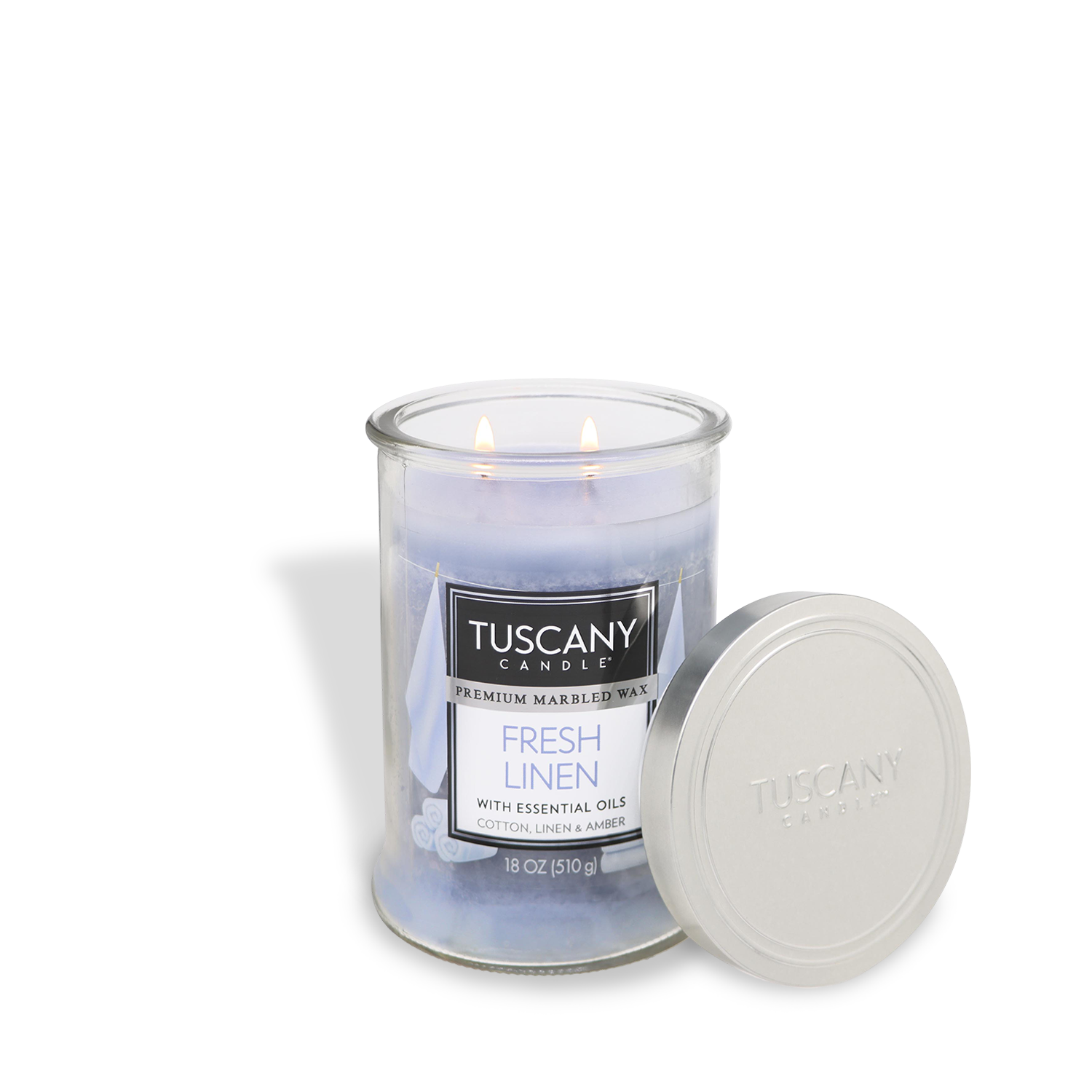 The Tuscany Candle® EVD "Fresh Linen" 18 oz scented jar candle, known for its long-lasting aroma and infused with essential oils, is lit with the silver lid placed beside it.