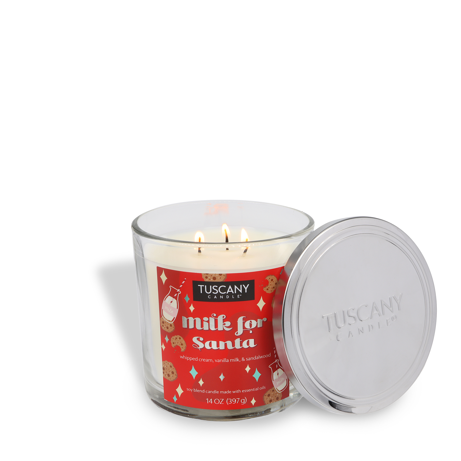 A lit Tuscany Candle® SEASONAL "Milk for Santa Scented Holiday Candle" (14 oz) with a festive red design, cookies and milk illustrations, and a metal lid next to the glass jar.
