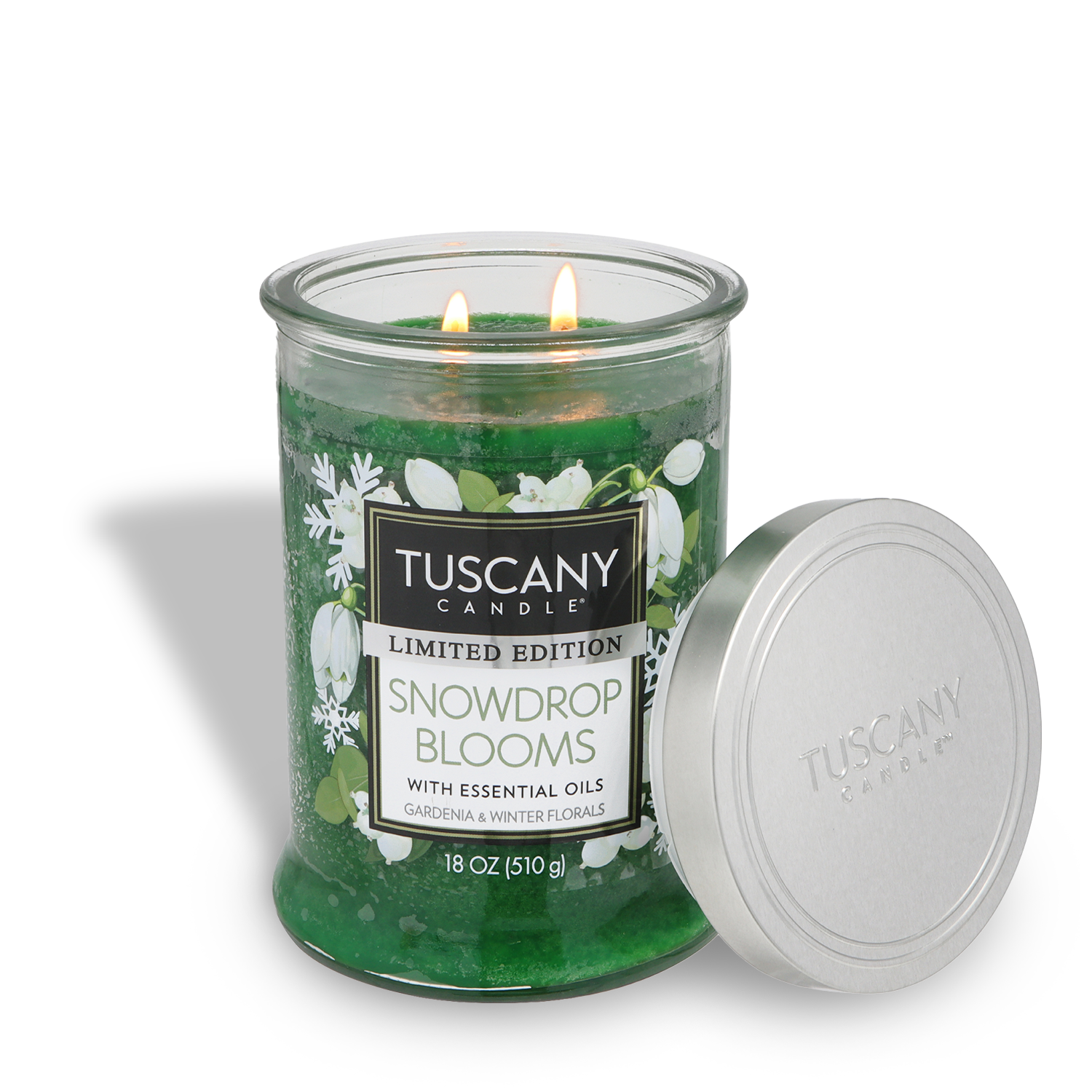 A green 18 oz Tuscany Candle® SEASONAL "Snowdrop Blooms: Gardenia & Winter Florals" holiday candle with two lit wicks sits next to its silver, floral- and snowflake-embellished lid.