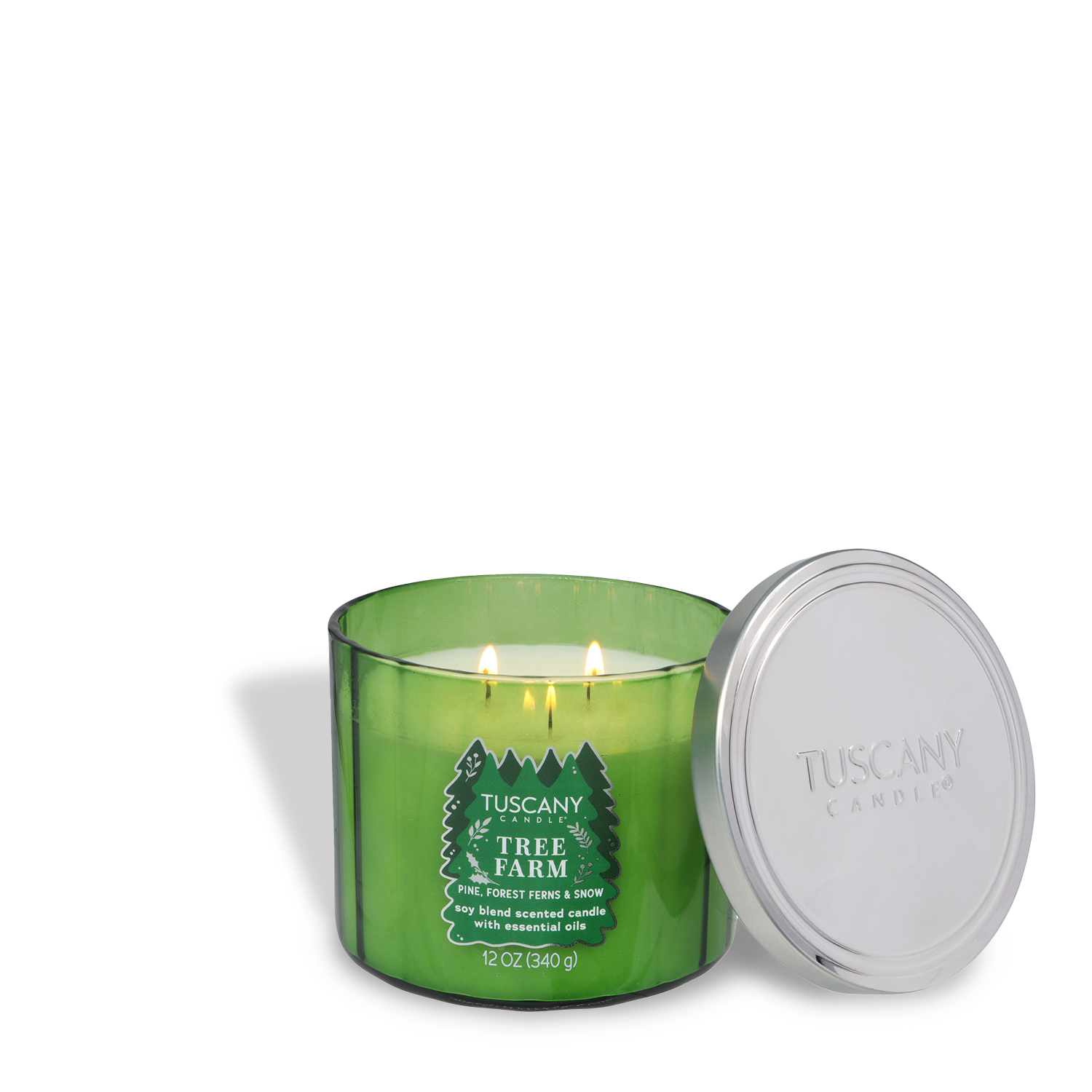 A green Tuscany Candle® SEASONAL "Tree Farm: Forest Ferns & Snow" 12 oz candle from the Winter Icons Collection, with two wicks lit, sits beside its silver lid on a white background.